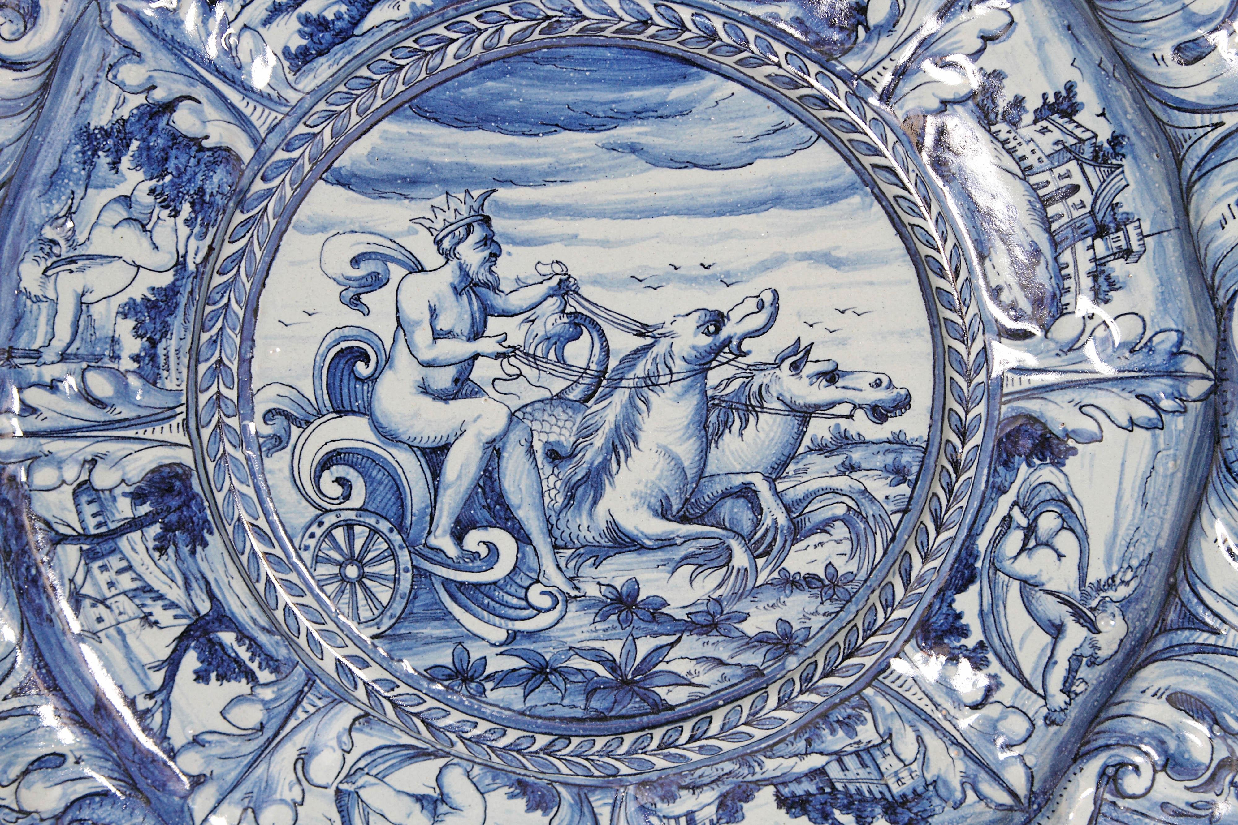 A large blue and white delft Faience charger. An elaborately shaped exterior rim surrounding a circle of alternating putti and castles. The center has a rimmed circle containing a scene of Neptune and his chariot, mid-19th century, Italy.