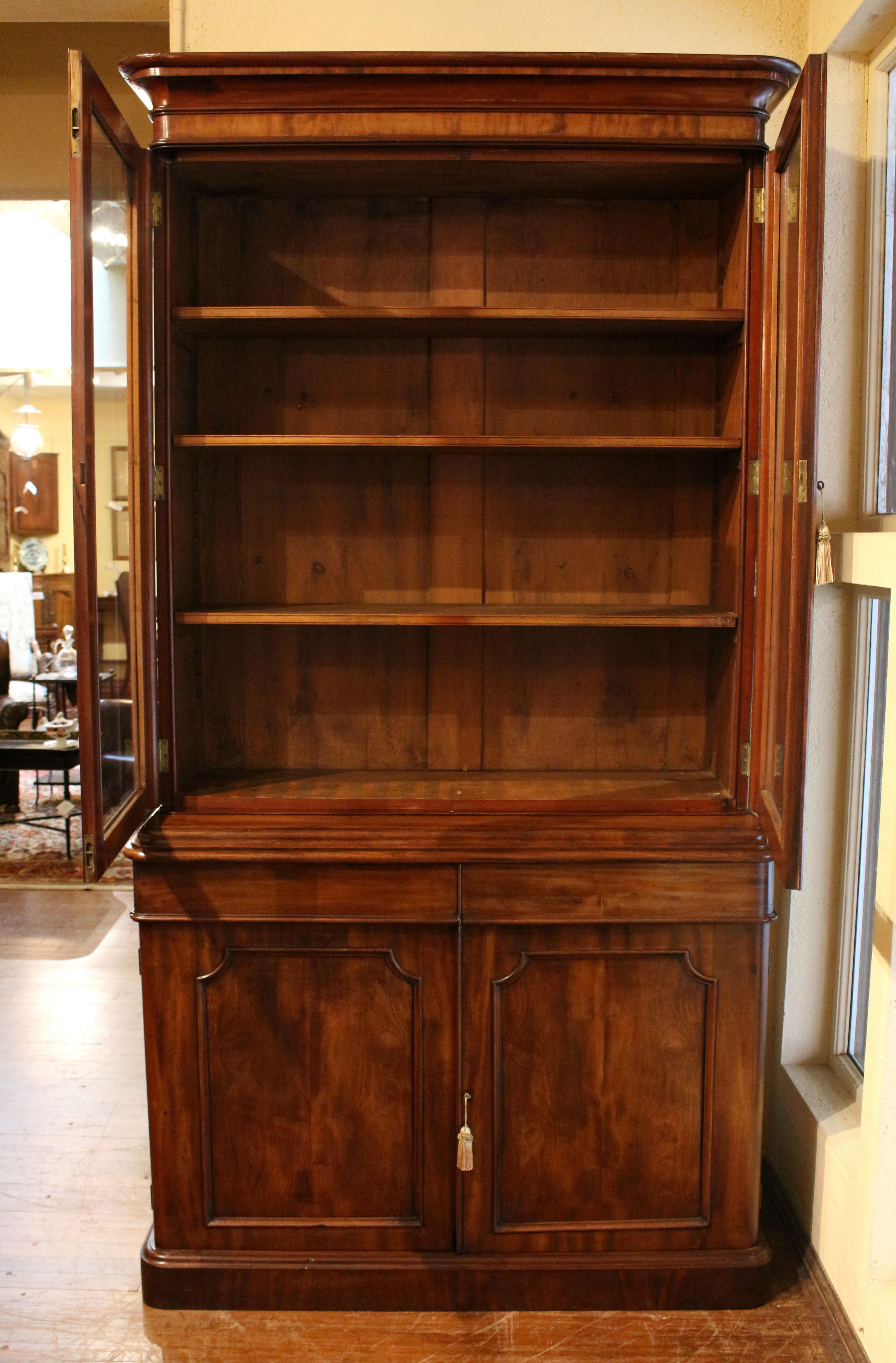 Mid-19th century bookcase cabinet, English. Cavetto corner molded doors - glass for upper section and blind for lower section. Adjustable shelve support bookcase section. Bold, ovolo molded crown. Bold ogee molded waist over 2 short drawers over