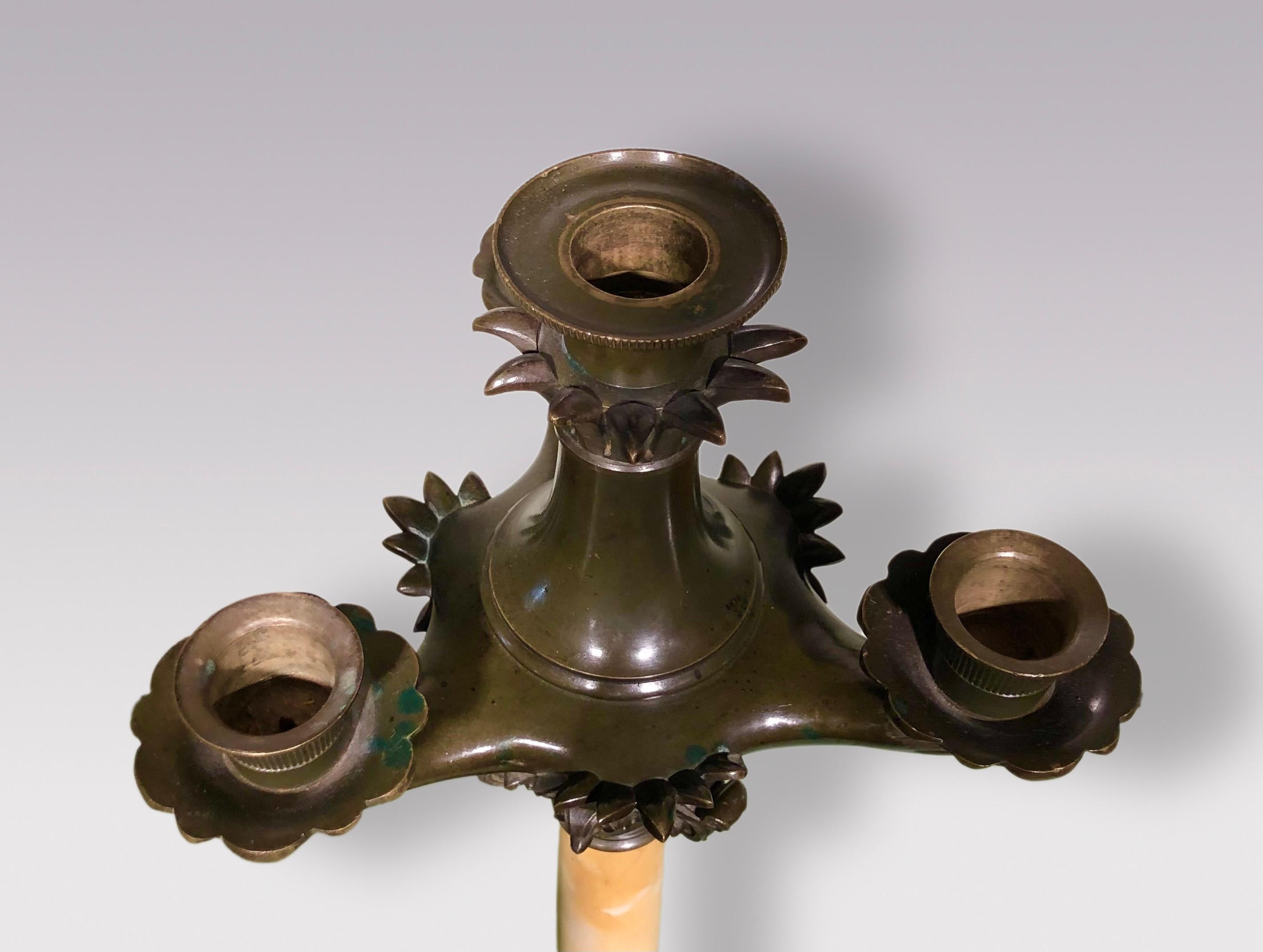 A mid-19th century bronze and sienna marble single four-light candelabrum, having leaf decorated sconces above stylized capital with tapered stem, supported on triple scroll feet, ending on concave triangular platform base.