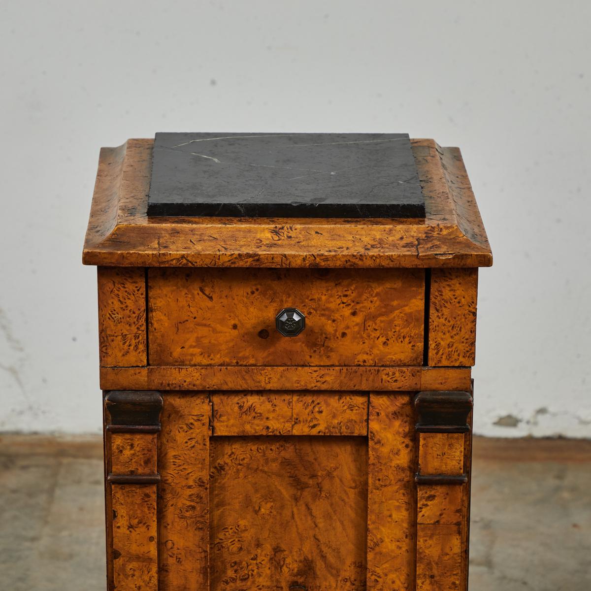 English mid-19th-century burled wood stand with black marble top, and single door storage. With petite iron handles and stained wood detailing, this piece makes a charming base for any sculpture or decorative object.

England, circa