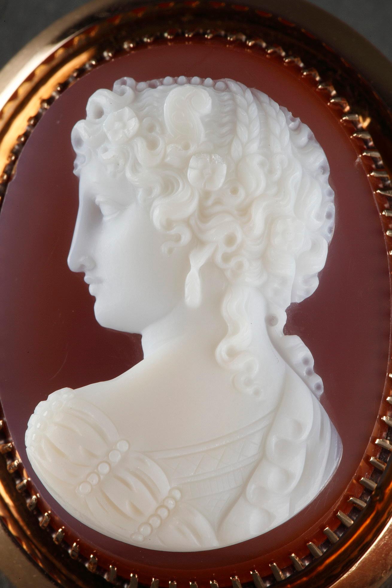 Pink Agate cameo depicting the bust of a young womanwith a Greek profile and looking on the left. She is wrapped in a tunic embellished with pearls. This hard stone is set in a gold frame.

If the art of the size of fine stone has existed since