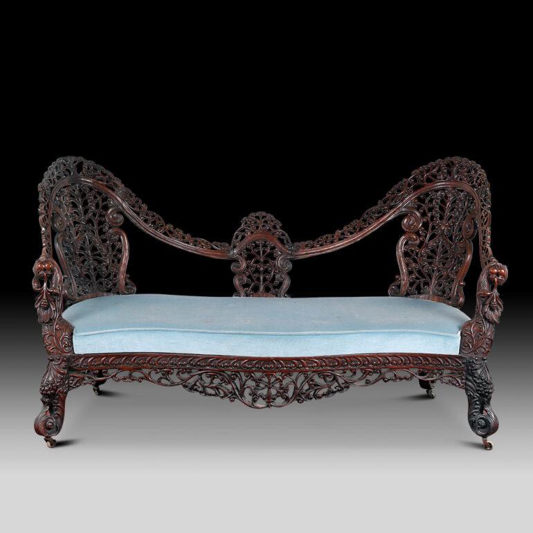 This is a beautiful hand carved hardwood Anglo Indian settee dates back to the mid Victorian era, circa 1860. The settee is of serpentine form, the profusely carved back is beautifully decorated with leaves and foliage. The arm rests terminate in