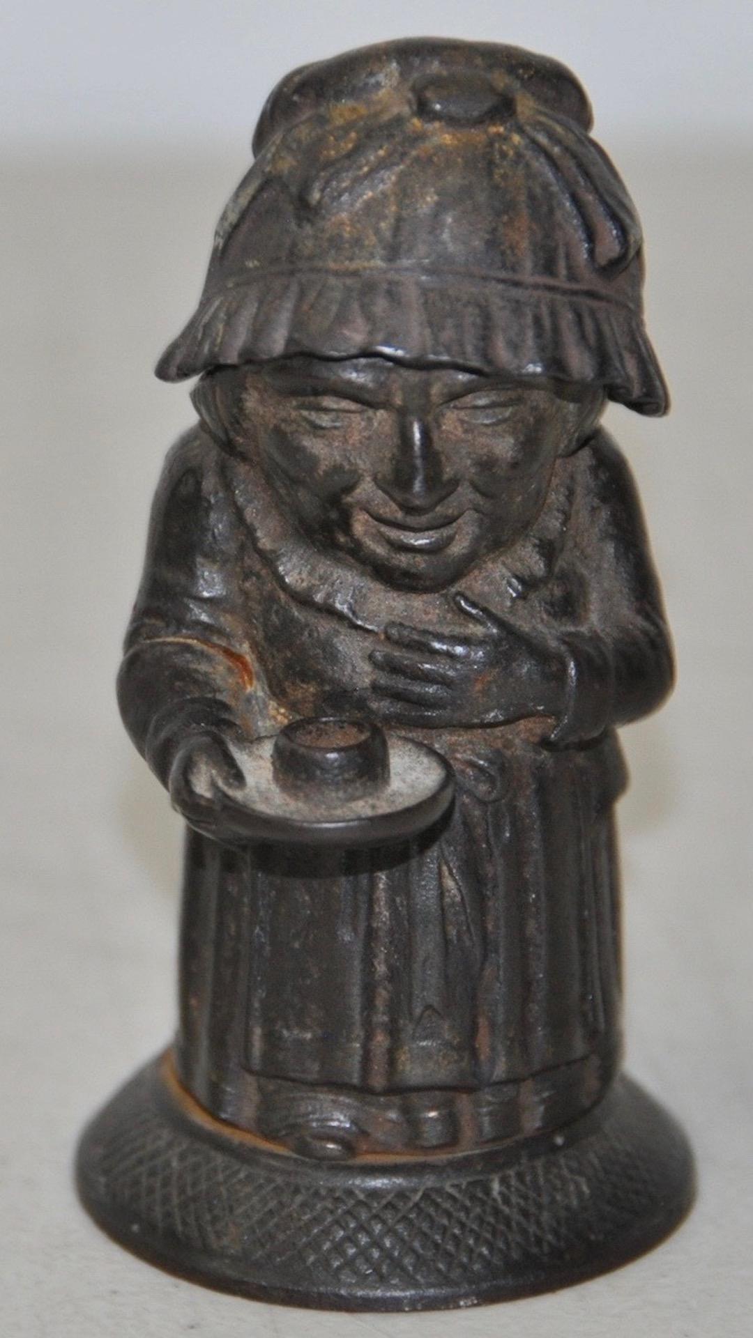 Rare mid-19th century cast iron match holder by Zimmerman of Hanau, Germany, circa 1850

This woman in her night clothes lights her way holding out her candle. Her cap removes to reveal an open space to store stick matches. A small candle will