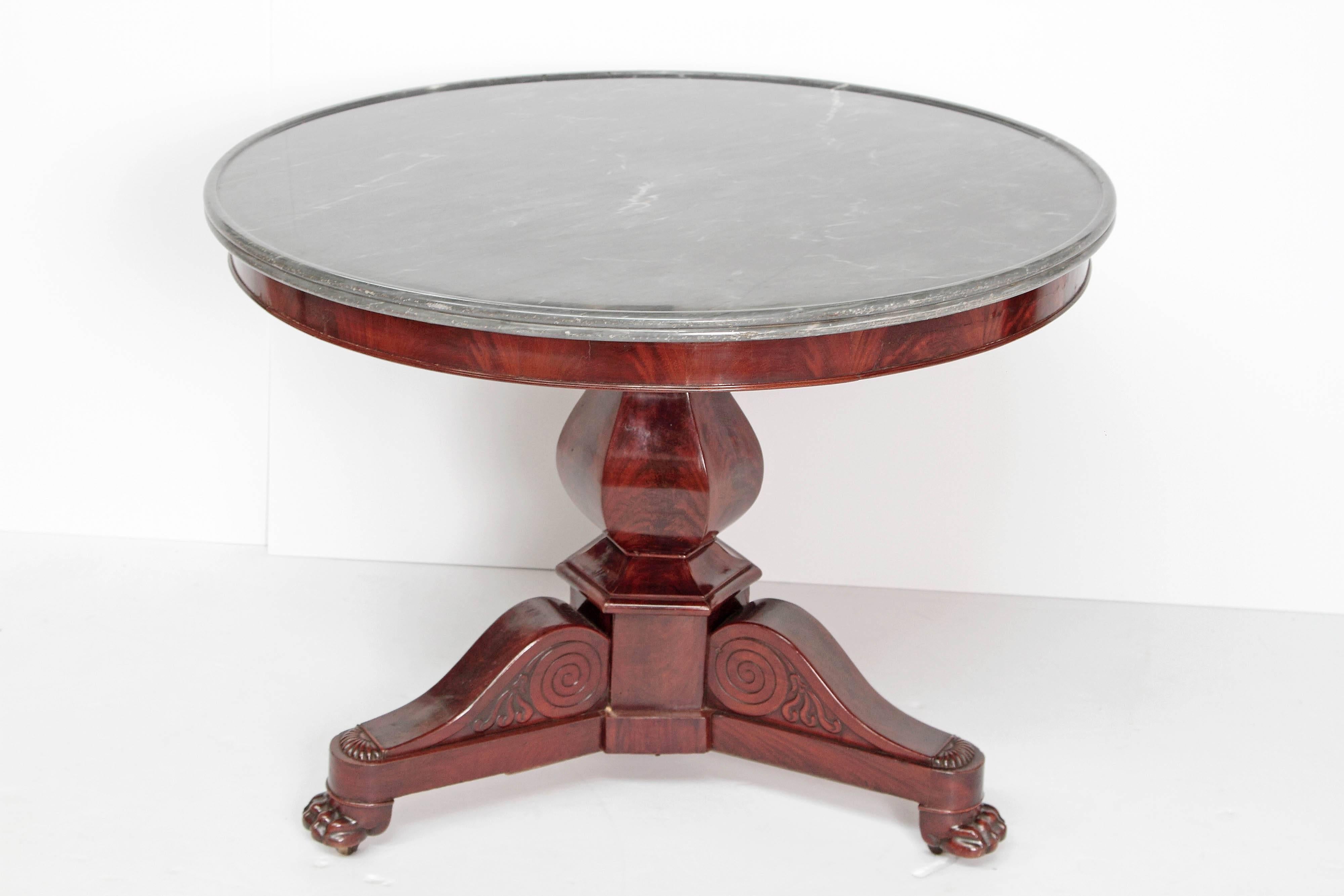 A Charles X center table of walnut. Grey marble top with ring at edge. Pedestal base with three extending legs with paw foot. Mid-19th century, France.