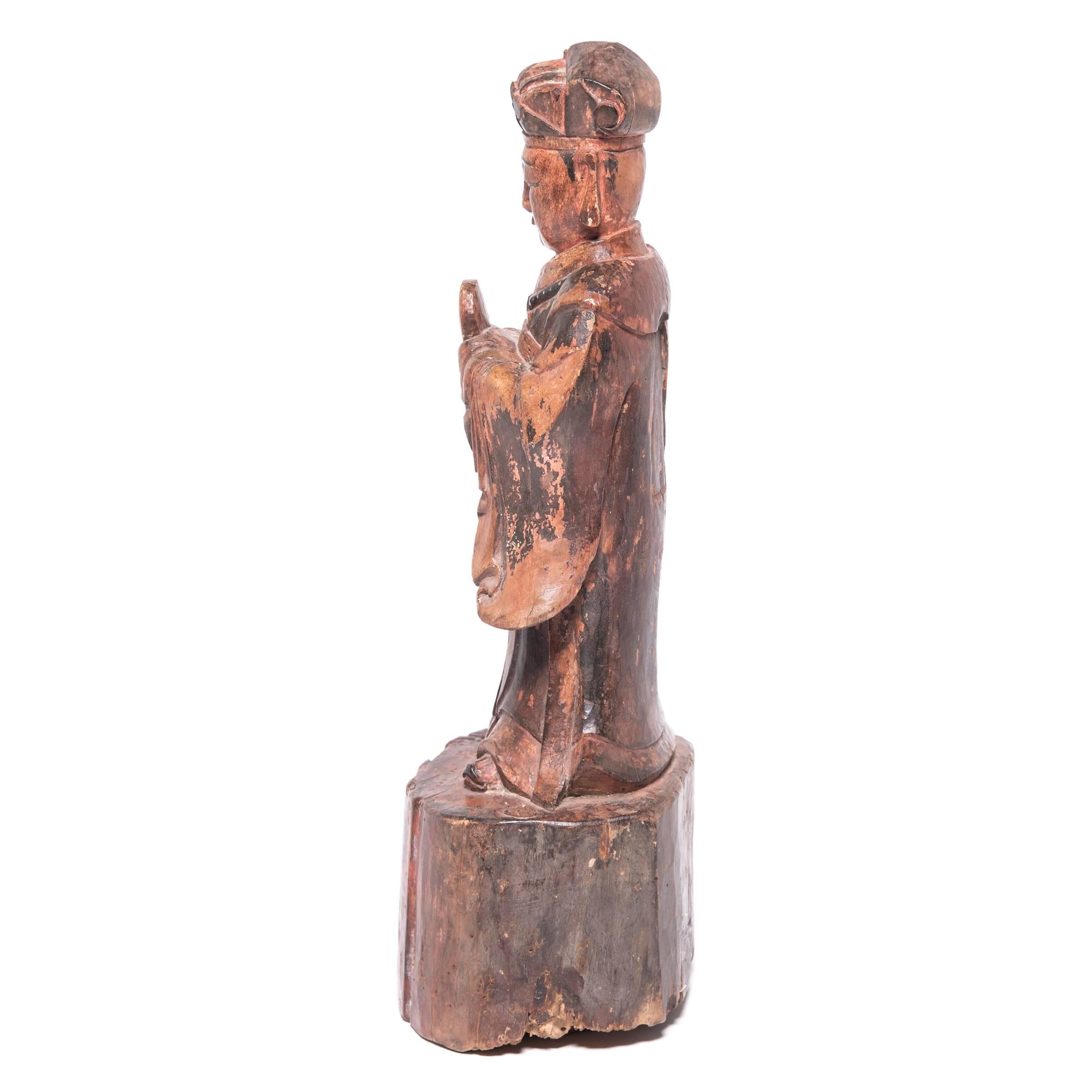 Carved in wood, this 19th century figure of a spirit paid tribute to ancestors past on a traditional altar table. Allowing the base to reflect the wood’s natural state, the artist carved the figure with detailed robes and distinguishable features,