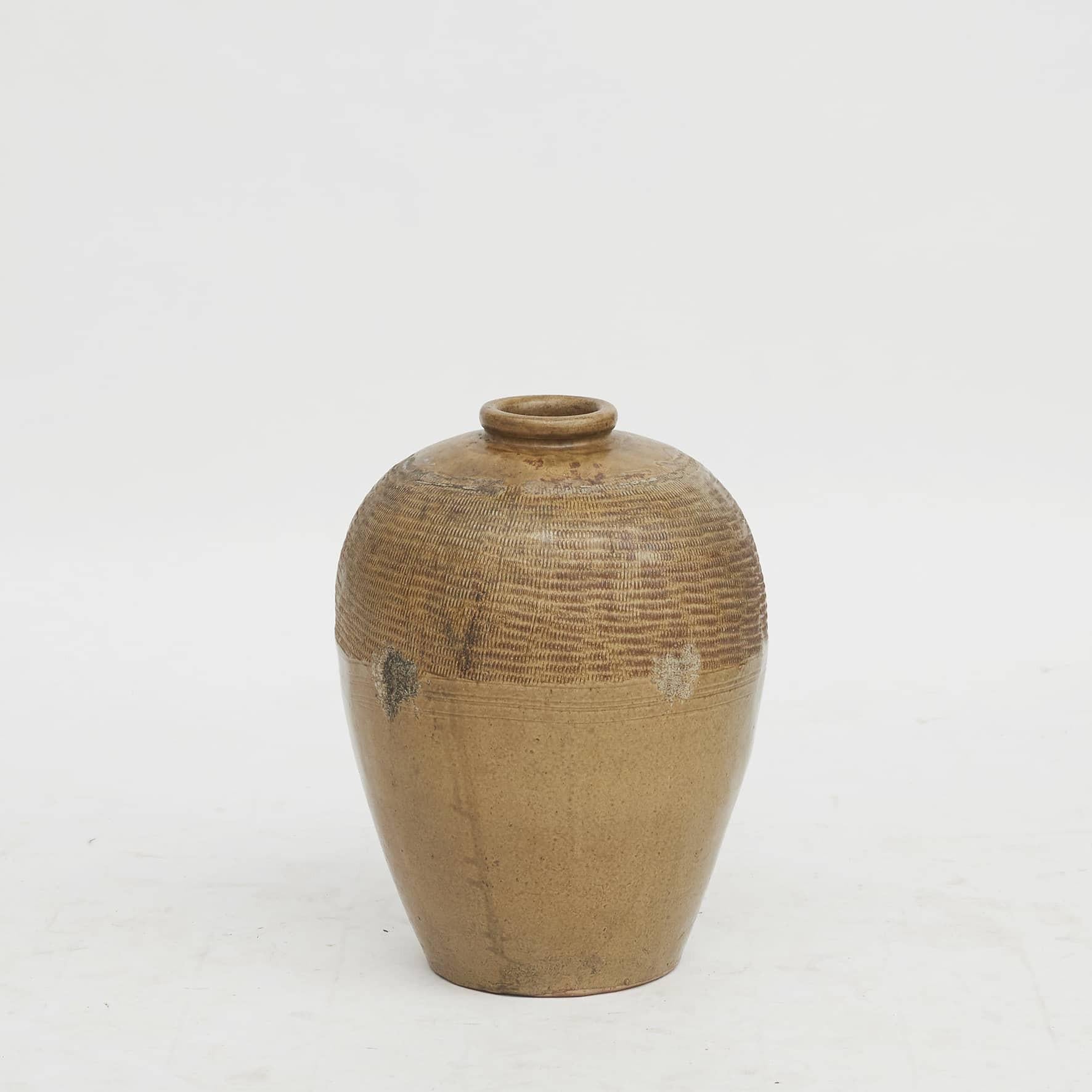 Chinese ochre glazed stoneware storage jar with a subtle ridged pattern along the top of the body.
Jars like this would have held wines, foods, and other consumable items.

China. Mid-19th century.