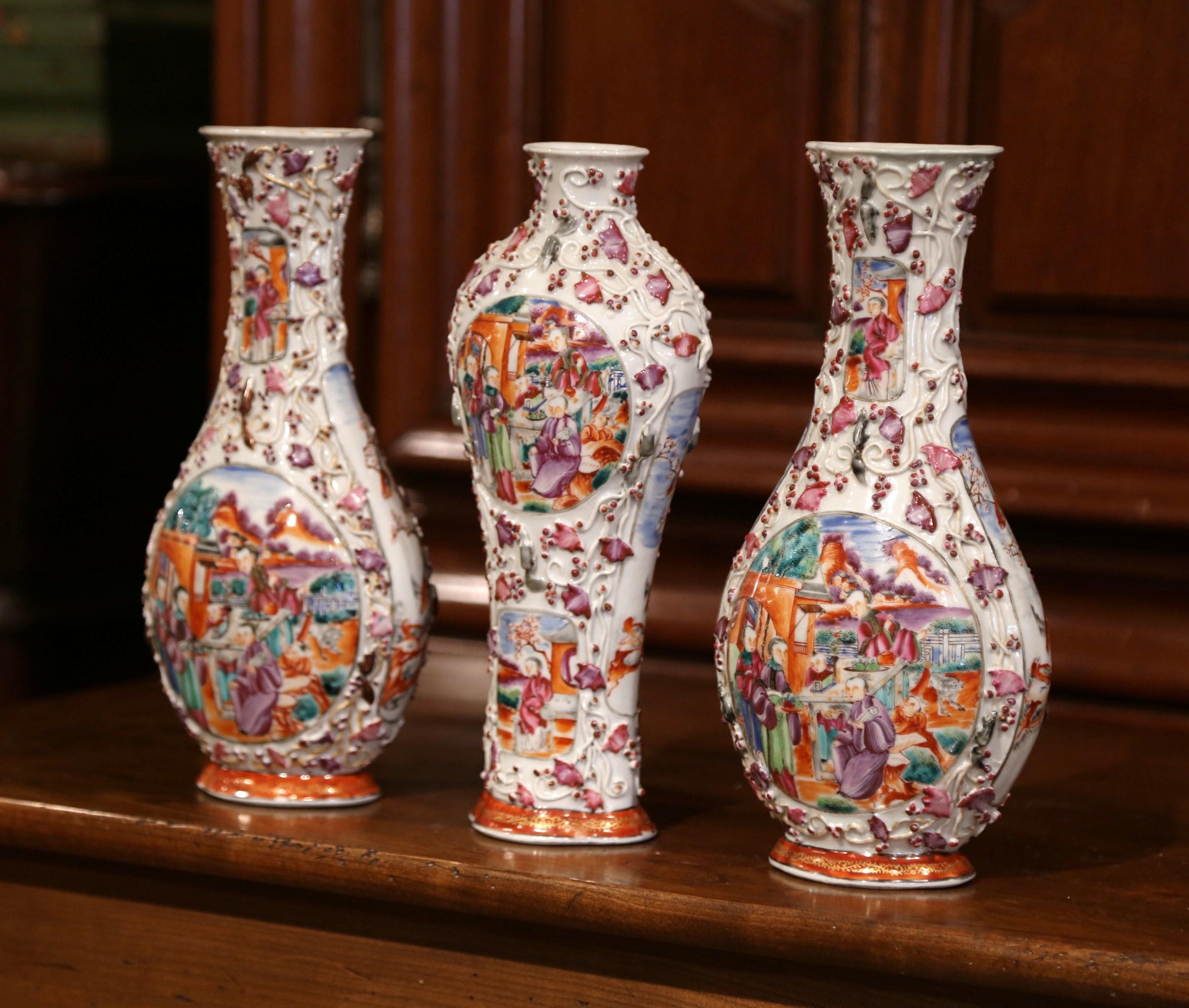 Decorate a mantel with this colorful garniture set of three Chinese export porcelain mandarin palette vases; crafted in China, circa 1850, the vases are in high relief and feature painted chinoiserie decor with figurative Mandarin scenes on both
