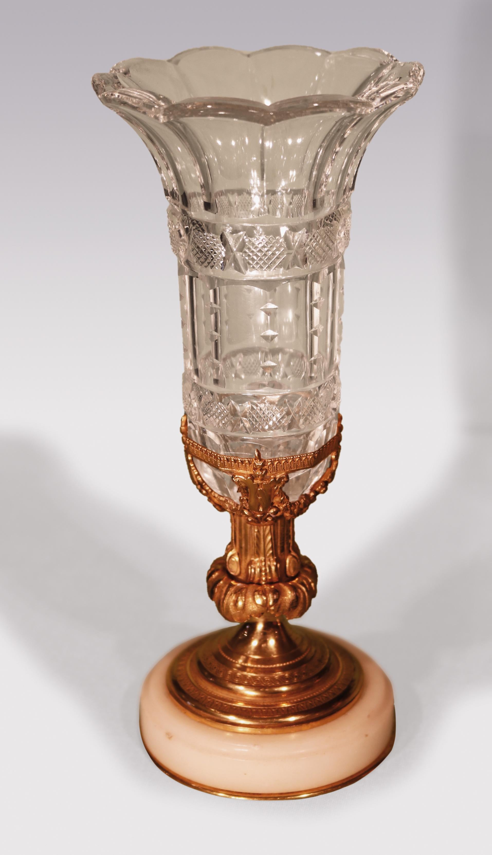 An unusual pair of mid-19th century cut-glass crystal vases having facetted borders and flared rims contained in intricately pierced ormolu holders, supported on acanthus and scroll stems ending on circular engine turned bases with white marble