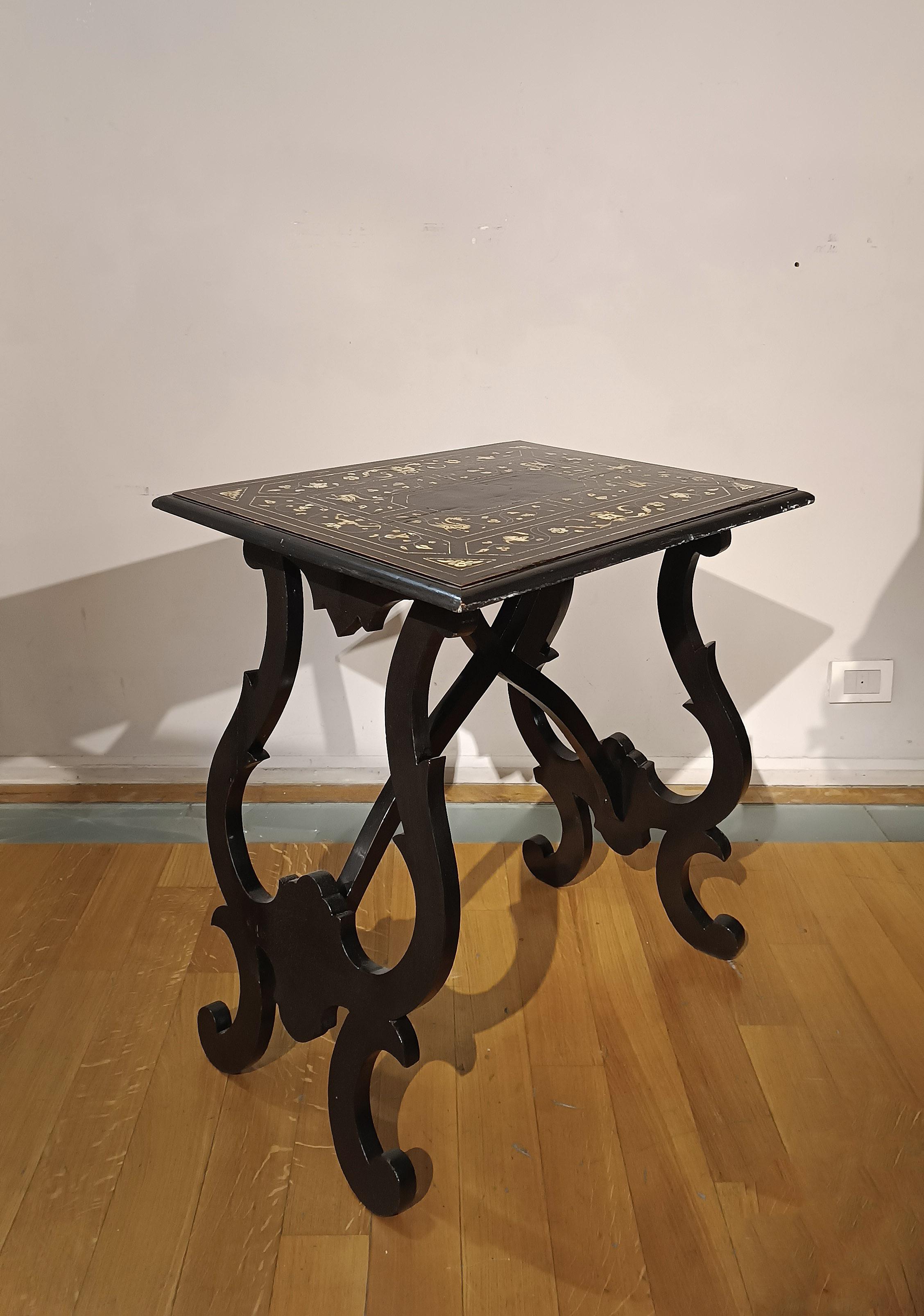 Elégante table basse en bois sculpté et ébonisé, avec incrustations et filets d'os sur le plateau. Les pieds en forme de lyre, caractérisés par une silhouette raffinée, sont soutenus par des traverses façonnées. La décoration du plateau se distingue