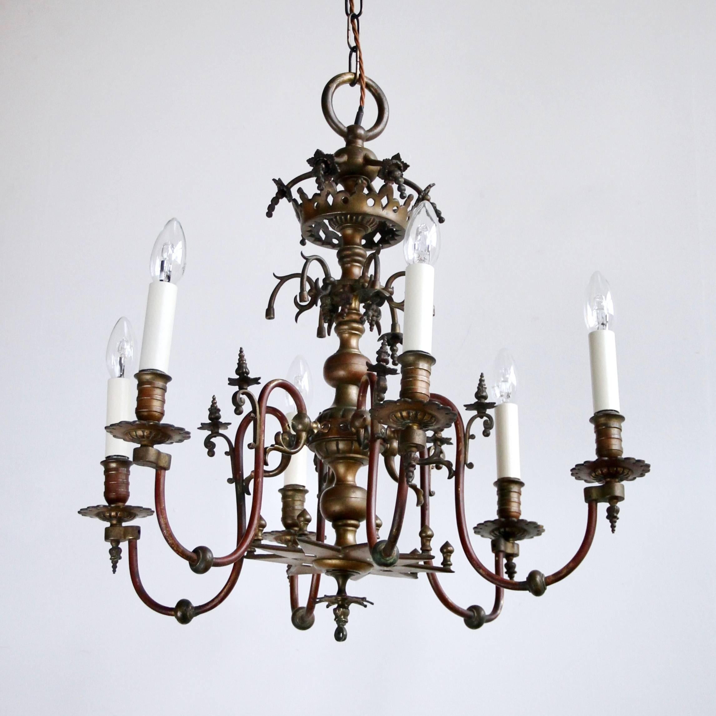 This electrified gasolier chandelier originates from the mid-19th century. The chandelier frame is made from bronze and copper and holds six lamps in total. With floral decorative bronze crowns and finials and the original rich burgundy paint on the