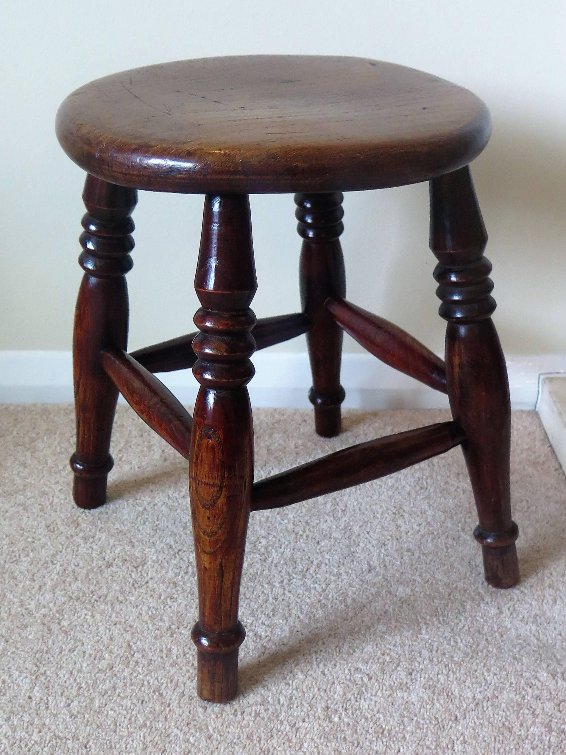 This is a lovely country stool made of Elm in Victorian England during the 19th century, circa 1850.

The elm stool has thick solid circular turned seat or top which sits on four ring turned legs with four shaped turned stretchers between the legs