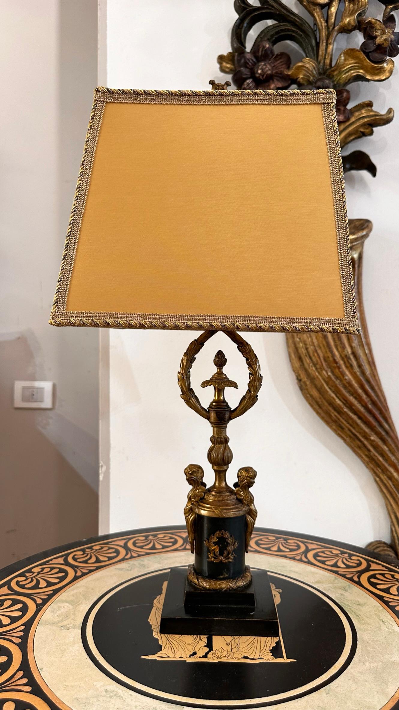 Elégante lampe de bureau à bouillotte d'époque Empire. La tige, en bronze à patine verte, est décorée d'éléments phytomorphes (dont une pomme de pin au centre), d'une lyre au sommet et de deux érotes en miroir à la base. La base est également en