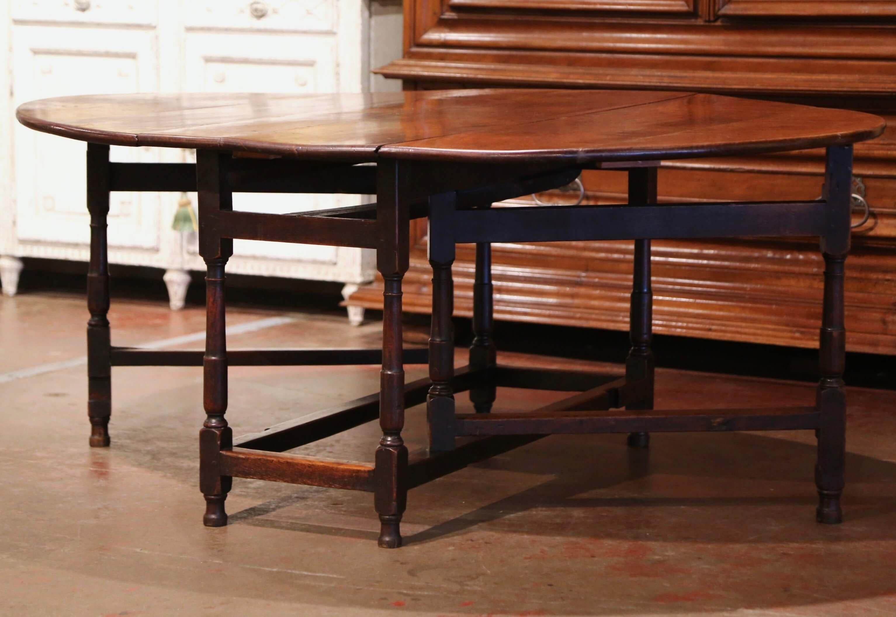 Crafted in England from solid oak circa 1850, the drop-leaf table stands on turned legs embellished with a decorative stretcher at the bottom. The table has four extra legs that unfold, and two large drop leaves come up to make an elegant oval top