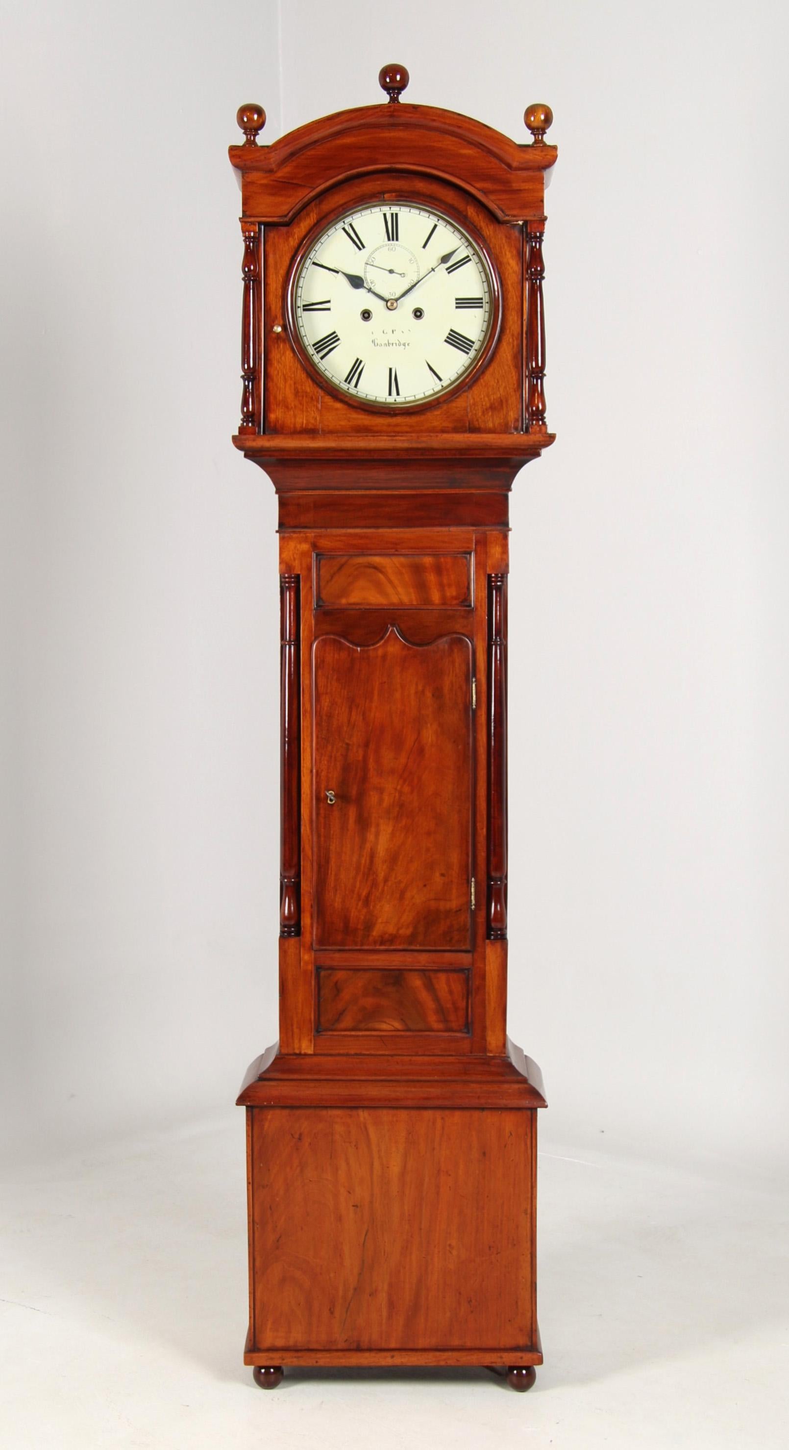 Antique English grandfather clock with painted dial in mahogany case

The case stands on small round feet and has a wide lower section, above which is a narrower section with a door and flanking half-columns, and a wide top section.

The white