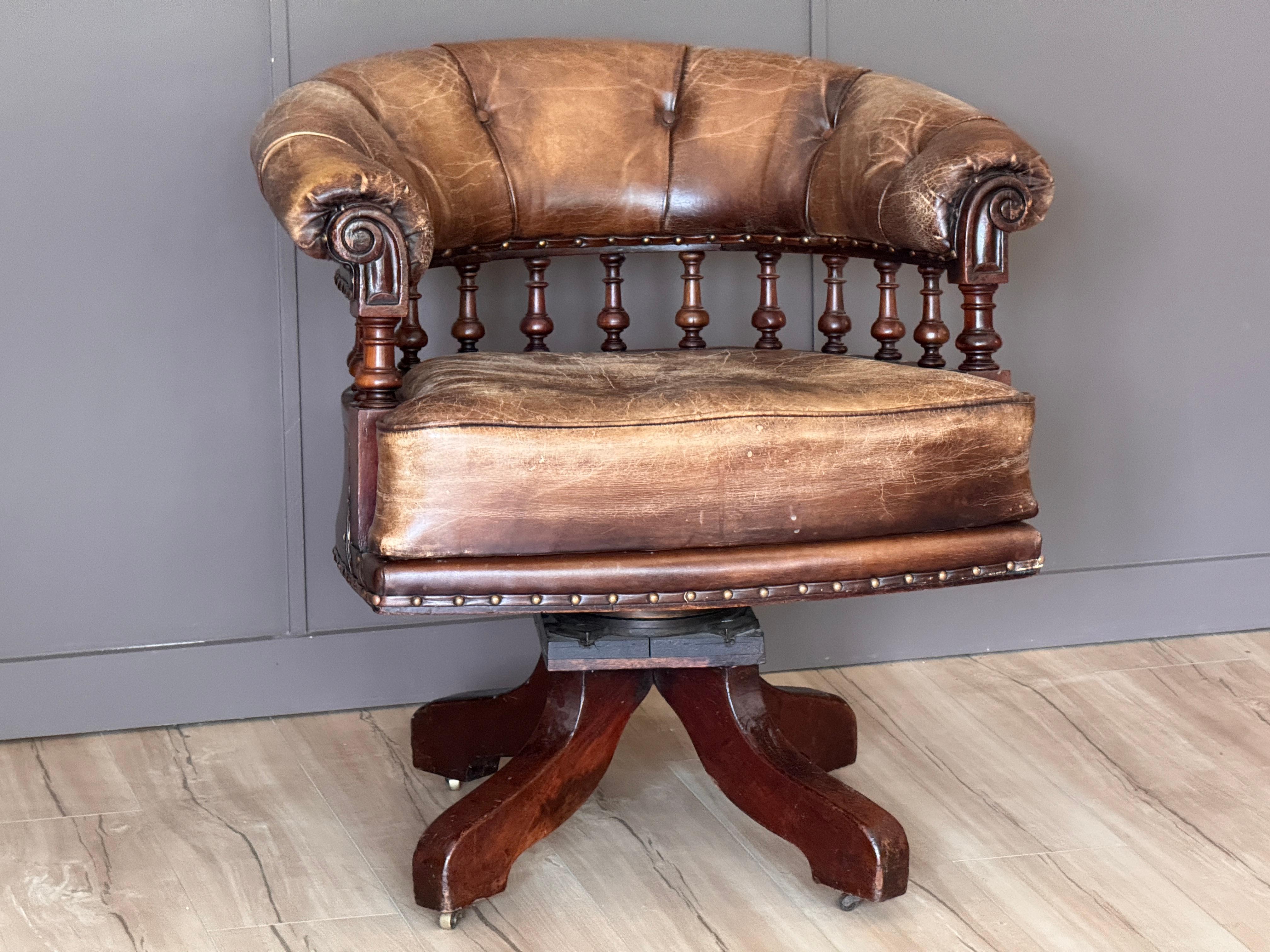 Bella e maschile sedia da scrivania in mogano inglese della metà del XIX secolo con rivestimento in pelle patinata, rotelle in ottone e supporti a fuso torniti. La sedia presenta un tradizionale schienale a botte con braccioli a voluta e decorazioni