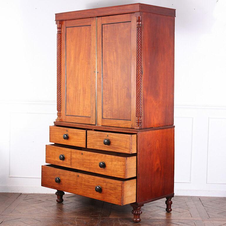 An English mid-Victorian linen press with two short over two long drawers to the base and removeable sliding open drawers fitted to the top cabinet, the whole raised on turned feet; the upper doors flanked with spiral turned columns. Solid mahogany