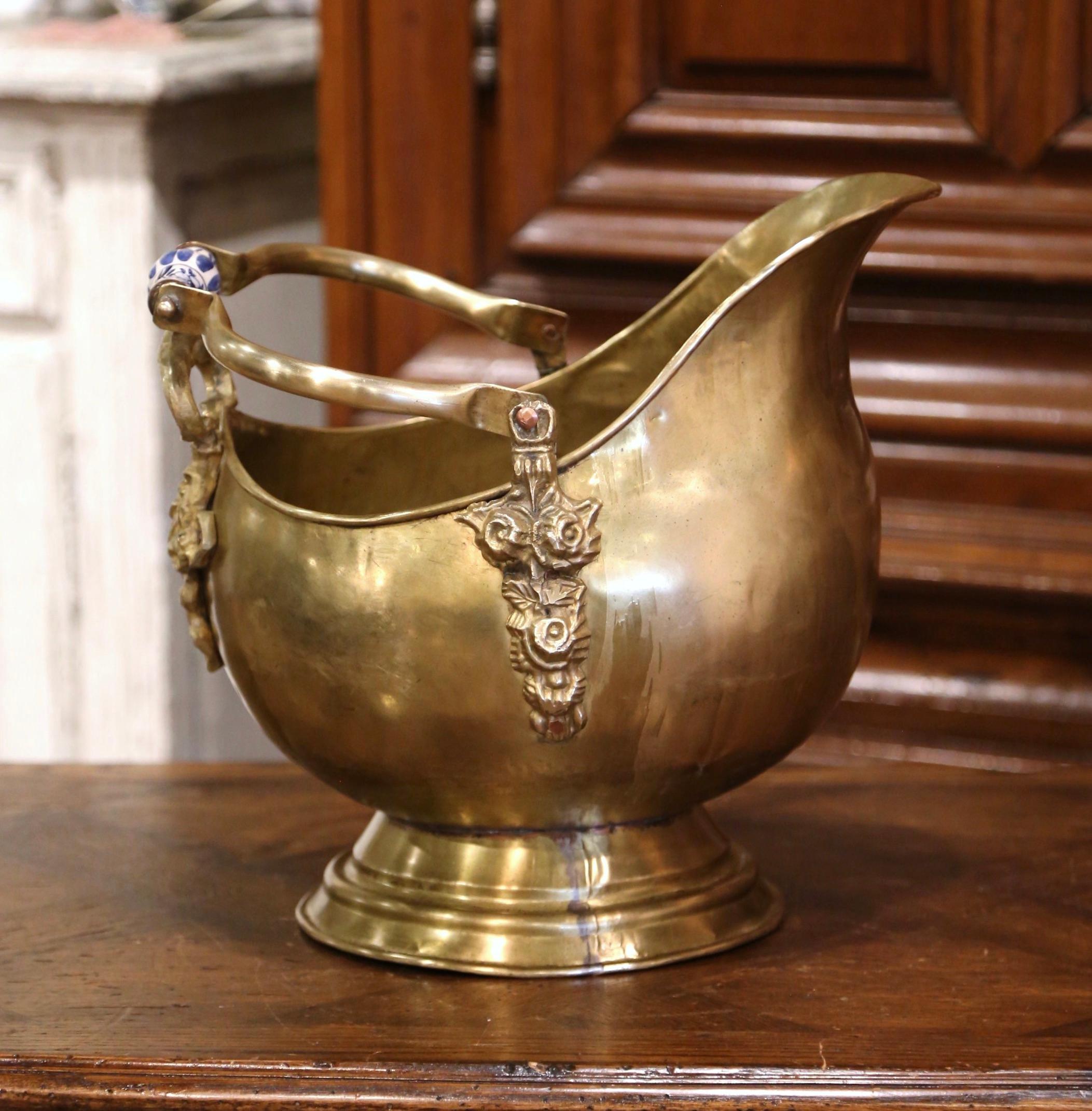 This antique coal scuttle was created in France, circa 1870. Built of brass with decorative floral bronze mounts and a hand painted blue and white porcelain handle, the oblong bucket stands on a round base. The versatile decorative box is in