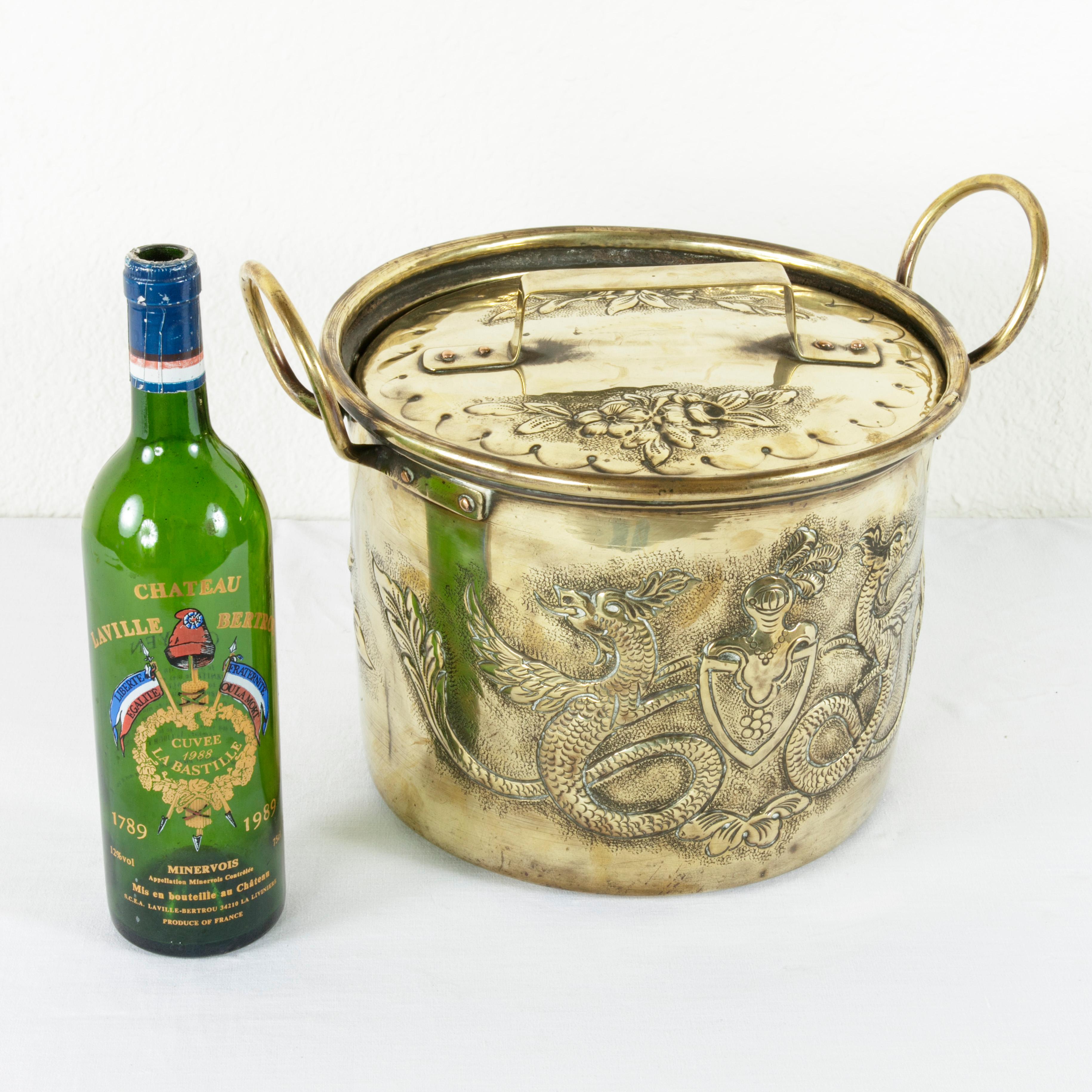 Originally used in a French chateau, this mid-19th century brass repousse pot features a coat-of-arms flanked by dragons on one side and a basket of flowers on the opposite side. The hand-hammered background surrounding the repousse work gives depth