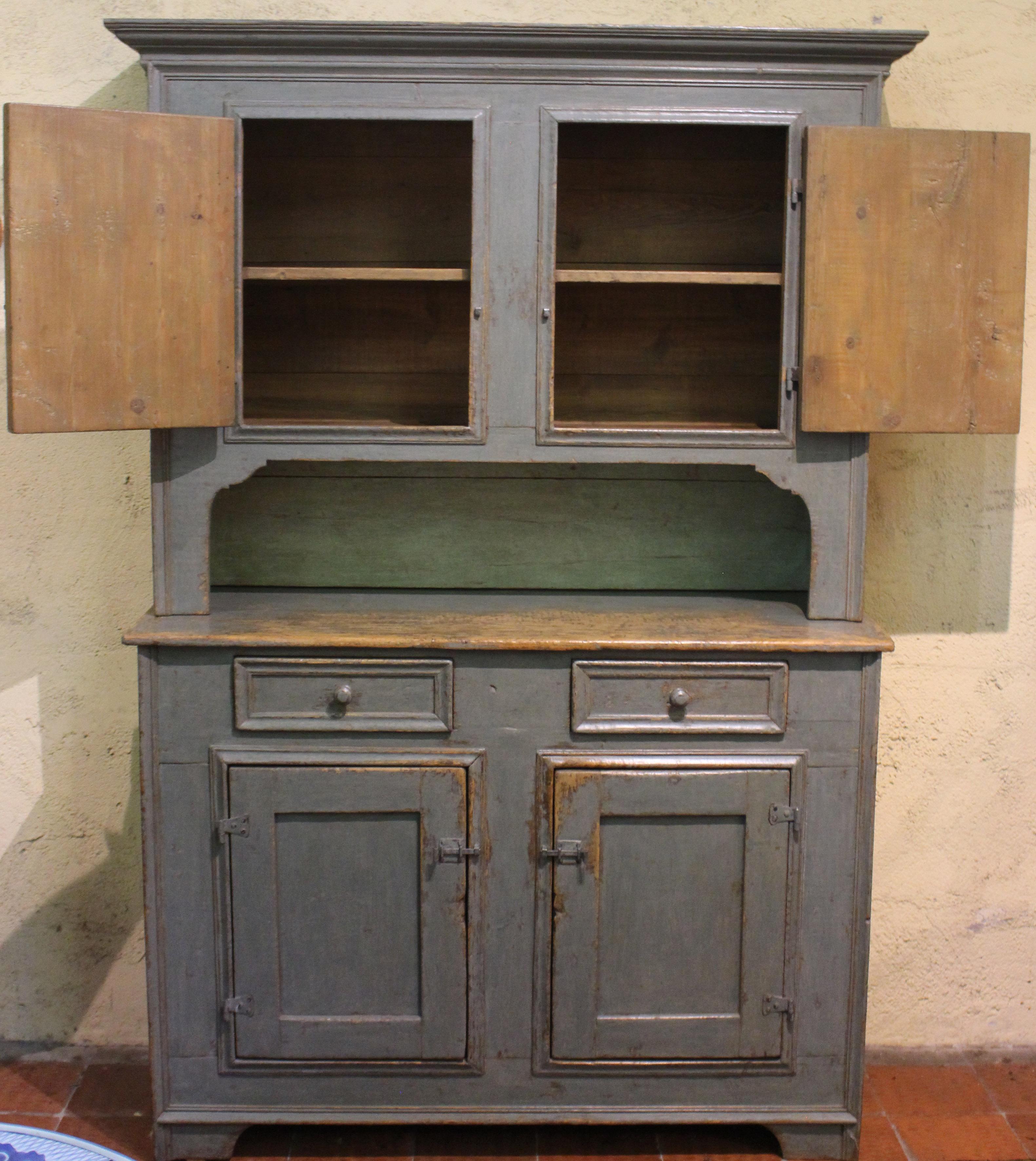 Mid-19th century country hutch or buffet à deux corps, French Canadian. Pine with wonderful old worn blue-grey paint. Panelled doors; upper section cut-out with shaped arches; bracketed feet; stepped, repetitive molding crown; turned knobs on the