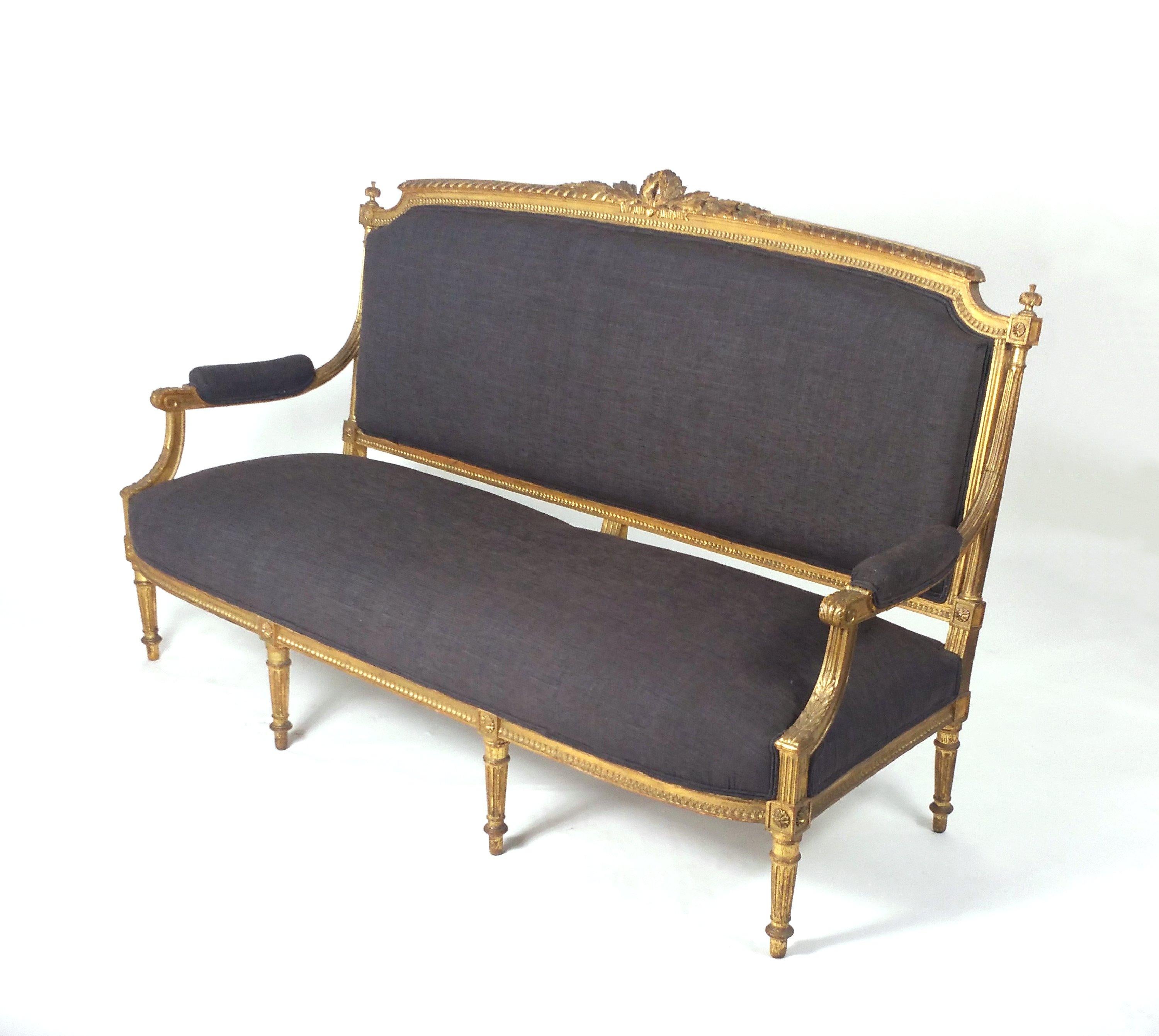 This elegant and very attractive mid-19th century French carved gilt wood sofa features ornate detailing and carving throughout, with acanthus leaves, ribbons, palmettes and scroll work. The sofa is upholstered in textured dark charcoal grey
