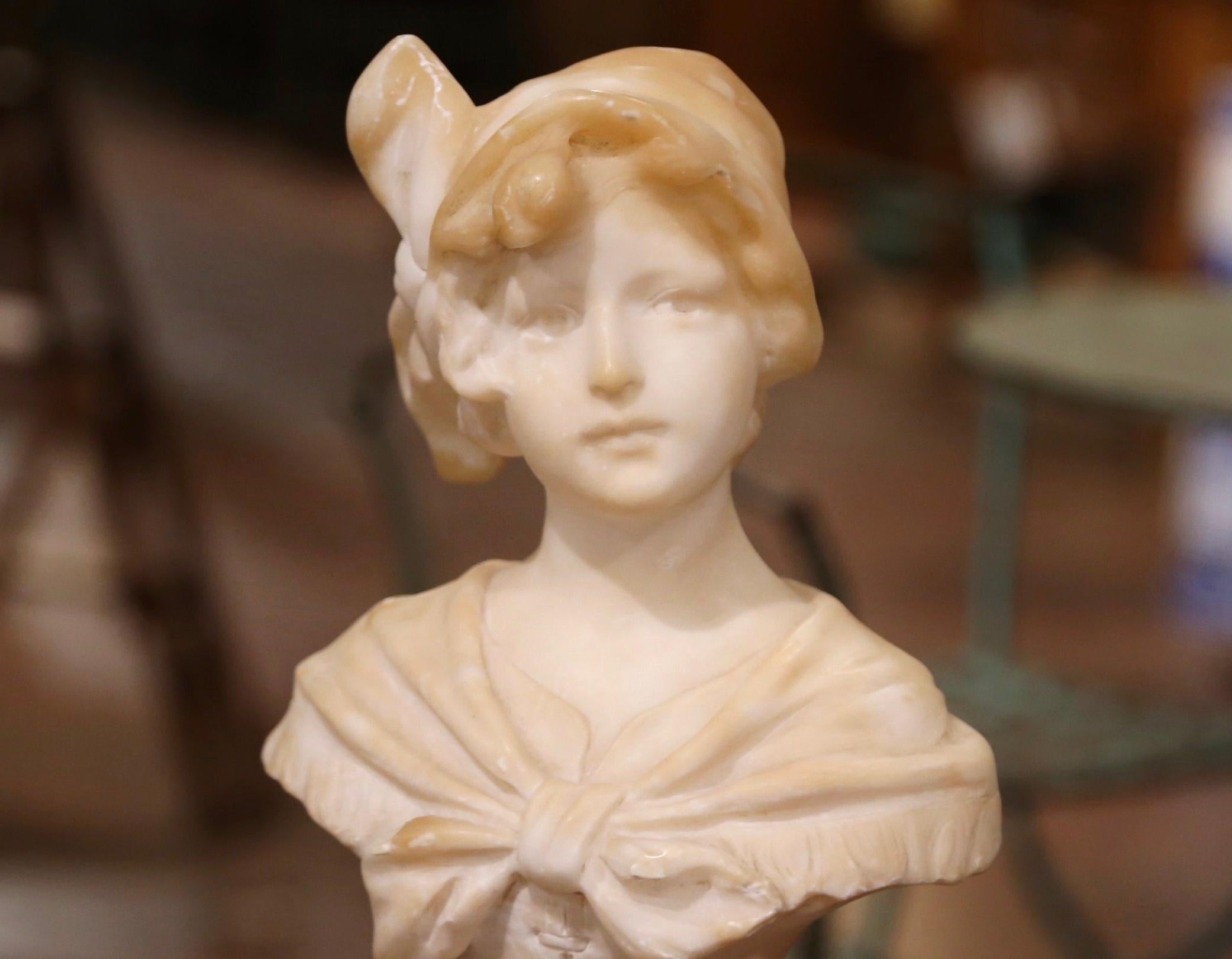 Crafted in France circa 1870, this antique marble bust is a true representation of French elegance. The figural sculpture features the visage of a beautiful, young girl wearing hat and side bow, and dressed in a corset under a shoulder shawl tied