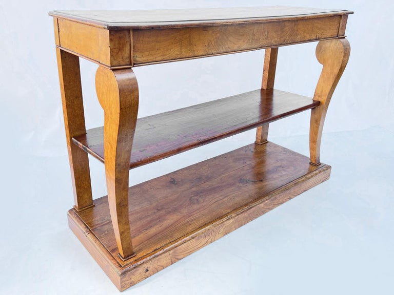 A French Empire elmwood console. Its rectangular top over a long, single-frieze drawer, raised on two curved and scrolled front legs joined by a shelf-stretcher, the entire piece rests atop a plinth base.

Stock ID: D1320.