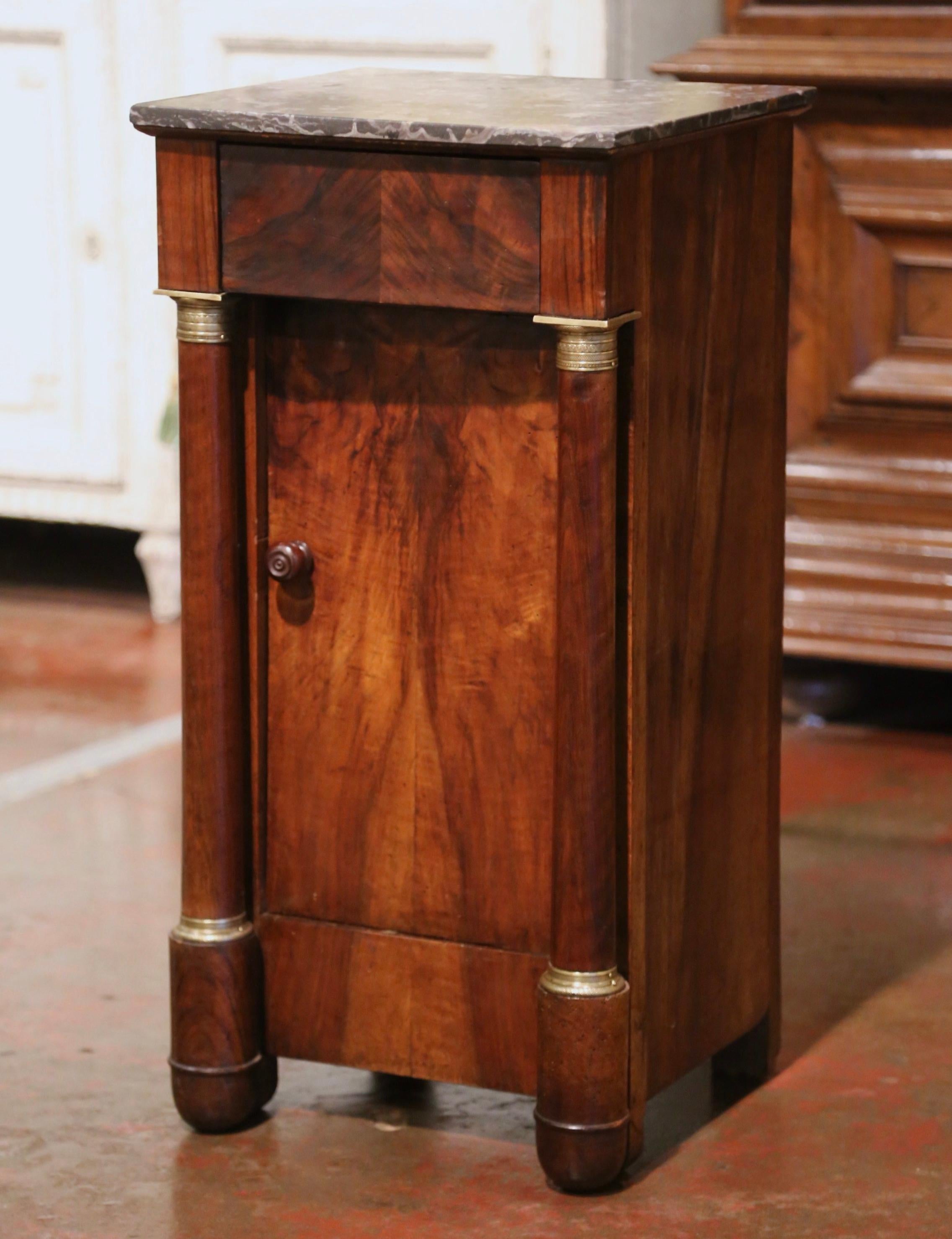 Crafted in France, circa 1870, the elegant antique cabinet stands on front rounded columns ending with bun feet and embellished with decorative brass mounts at the shoulder and the base; the small fruit wood chest features a drawer across the front