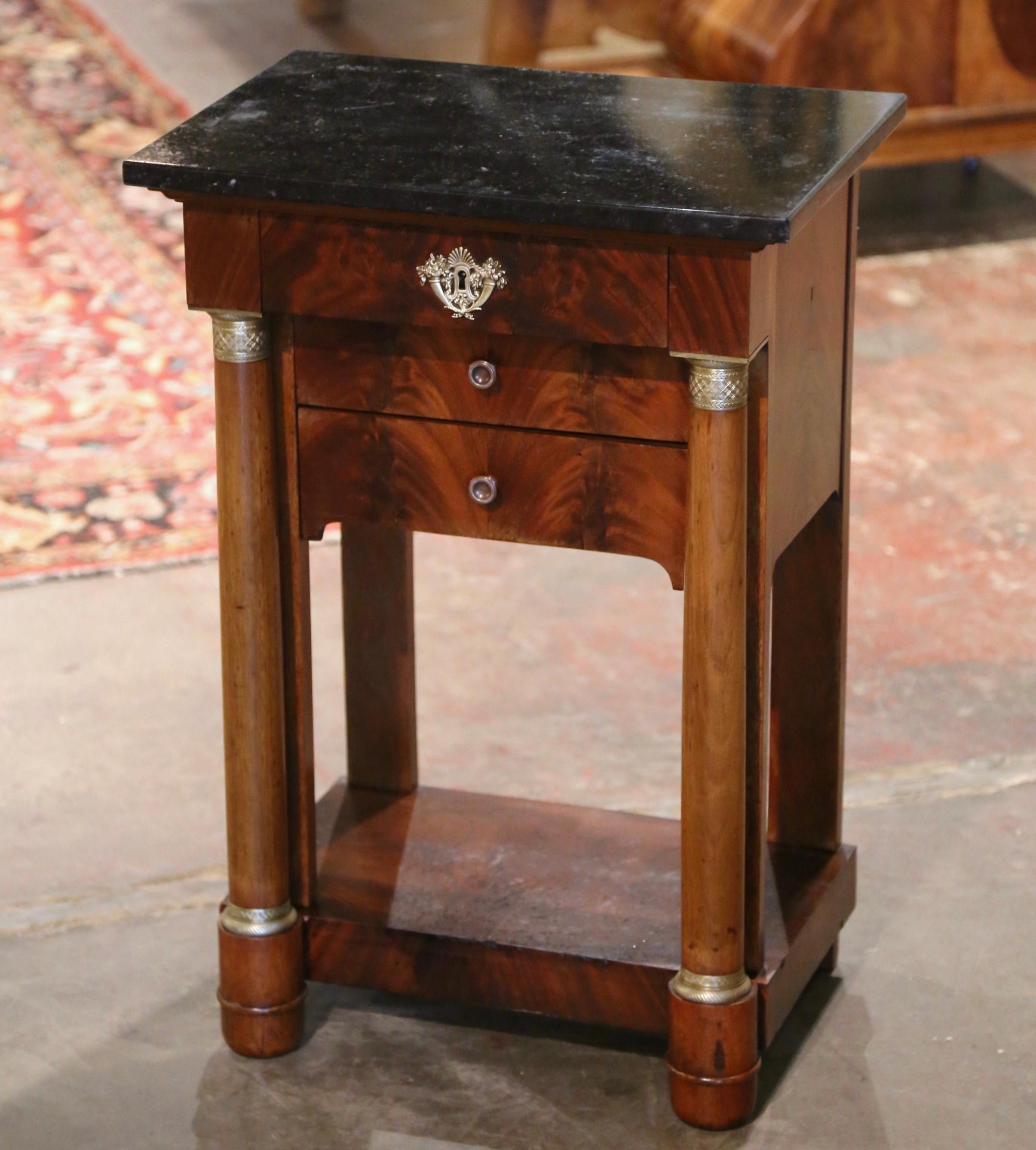 Crafted in France circa 1850 and built of mahogany, the elegant antique cabinet stands on front rounded columns ending with bun feet and embellished with decorative bronze mounted rings at the shoulder and the base; the small chest features three