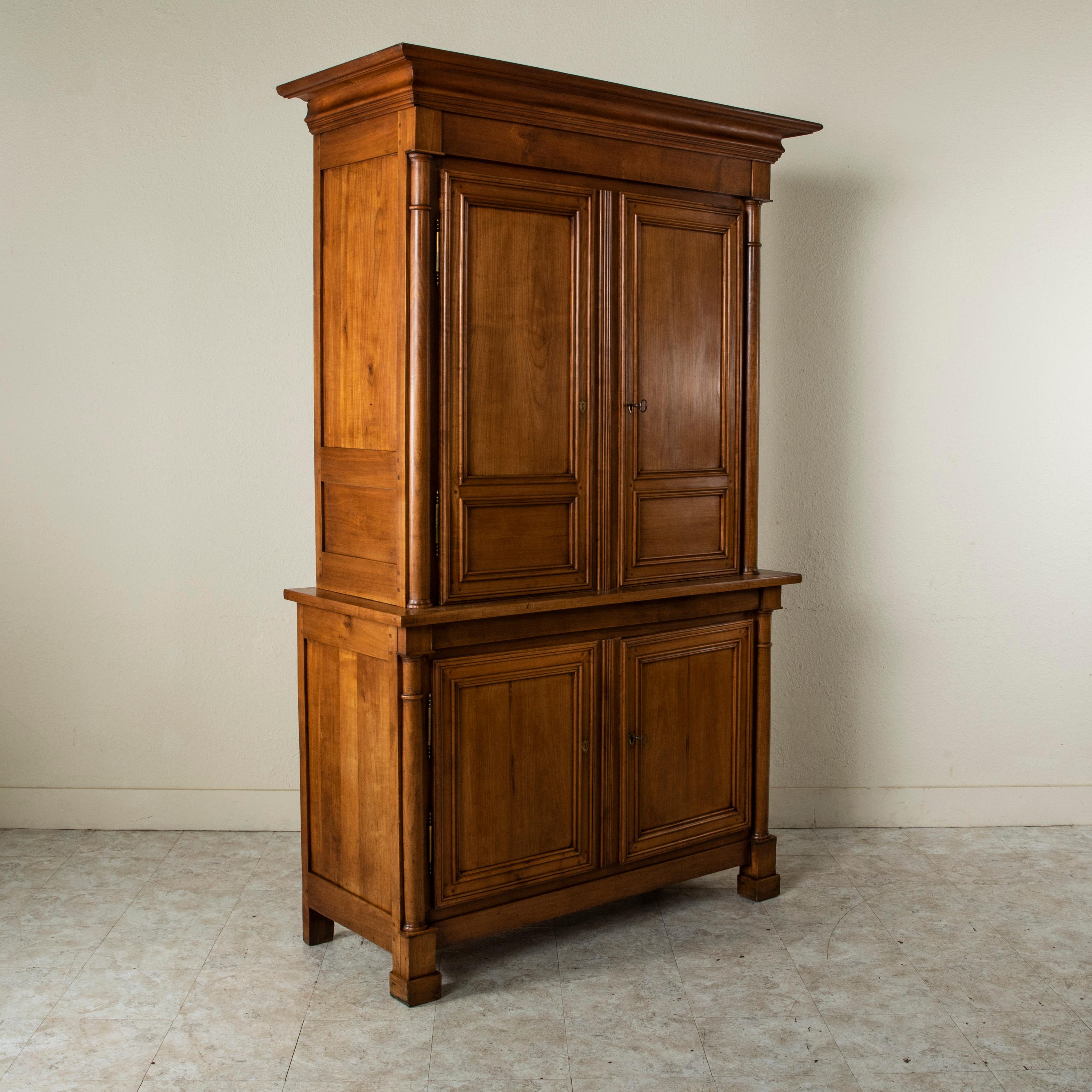 This mid-nineteenth century French Empire style hand pegged cherrywood buffet deux corps features classic half columns that flank both the upper and lower doors. The two doors to the upper cabinet open to reveal an interior with two shelves. Two