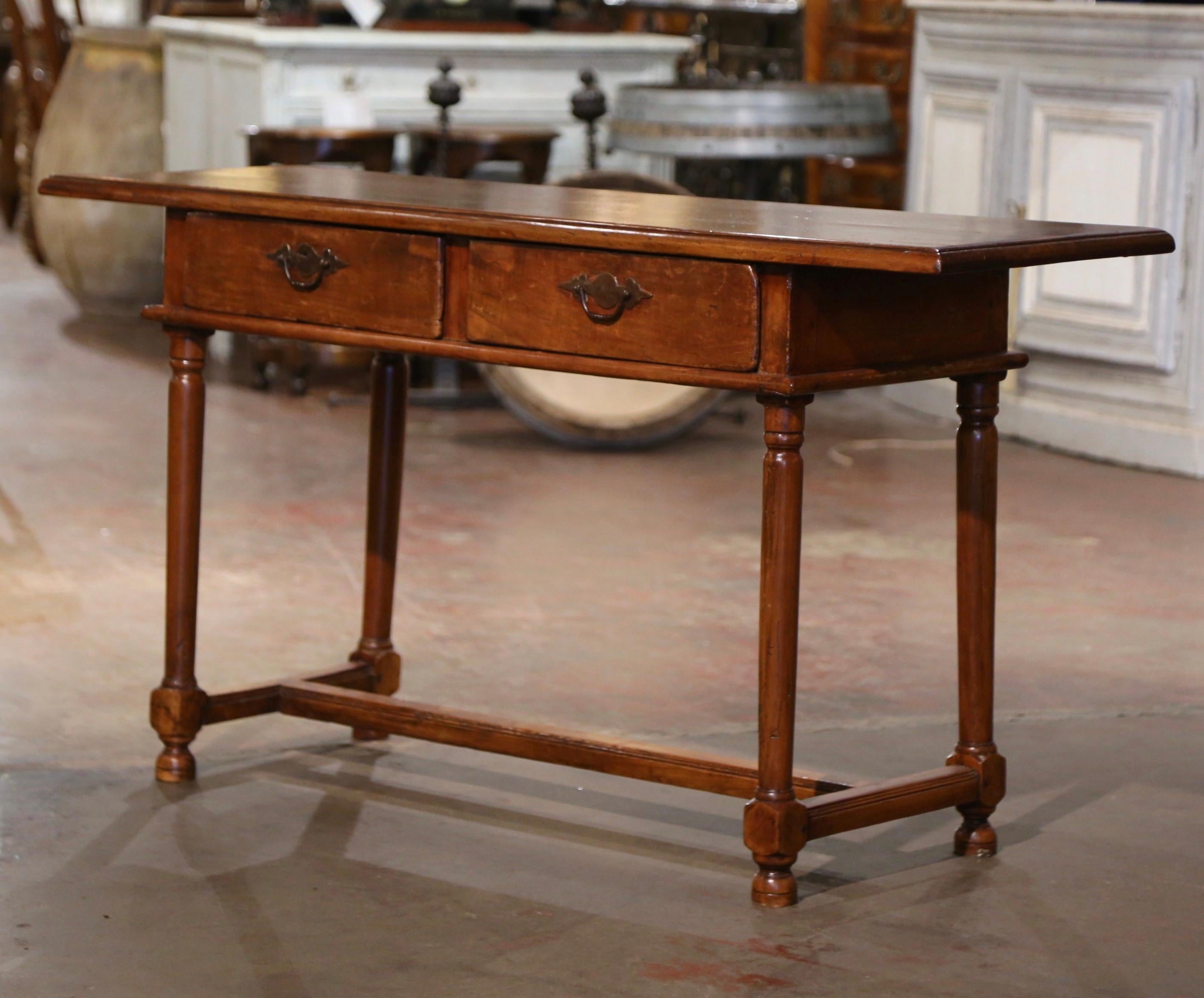 Dress an entryway or hall way with this elegant, antique console. Crafted in France, circa 1820, the simple, narrow, fruit wood table stands on four turned legs embellished with a bottom stretcher. The table features two drawers across the front