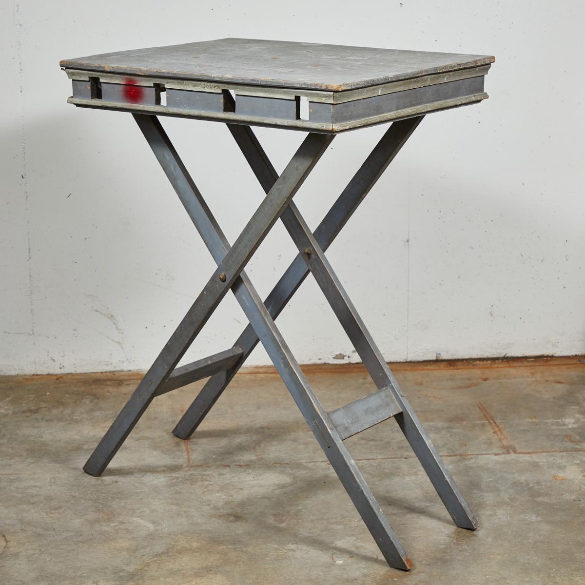 French 19th-century presentation table on foldable X-shaped platform. Industrial yet delicate, the piece is comprised of a gray painted wood rectangular top and metal base with stretcher supports, and retains trace remnants of paint and other