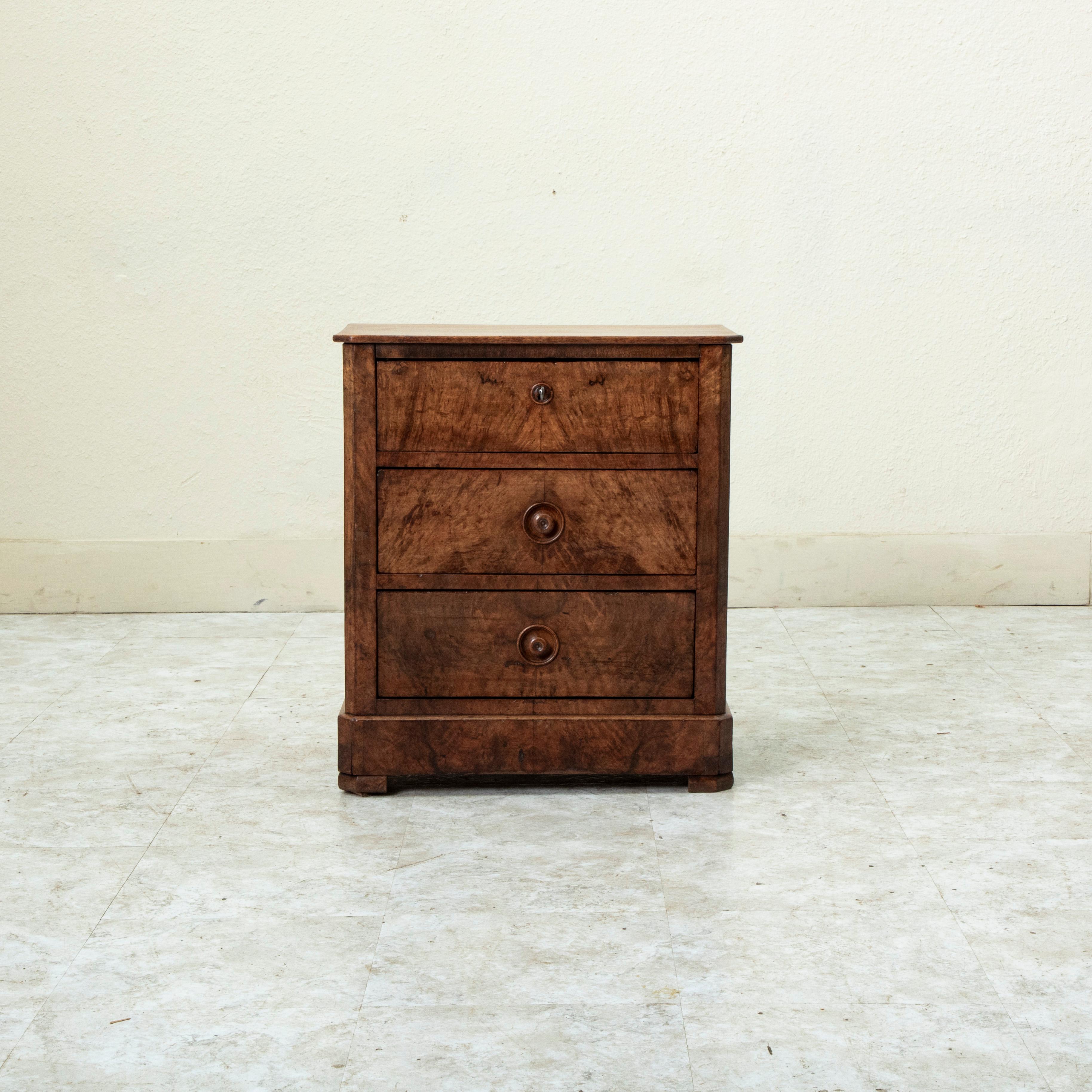 Rare for its smaller scale with a 21 inch width, this nineteenth century Louis Philippe period chest of drawers features a facade of book matched burl walnut. Its three drawers of dovetail construction are appointed with hand turned drawer pulls for
