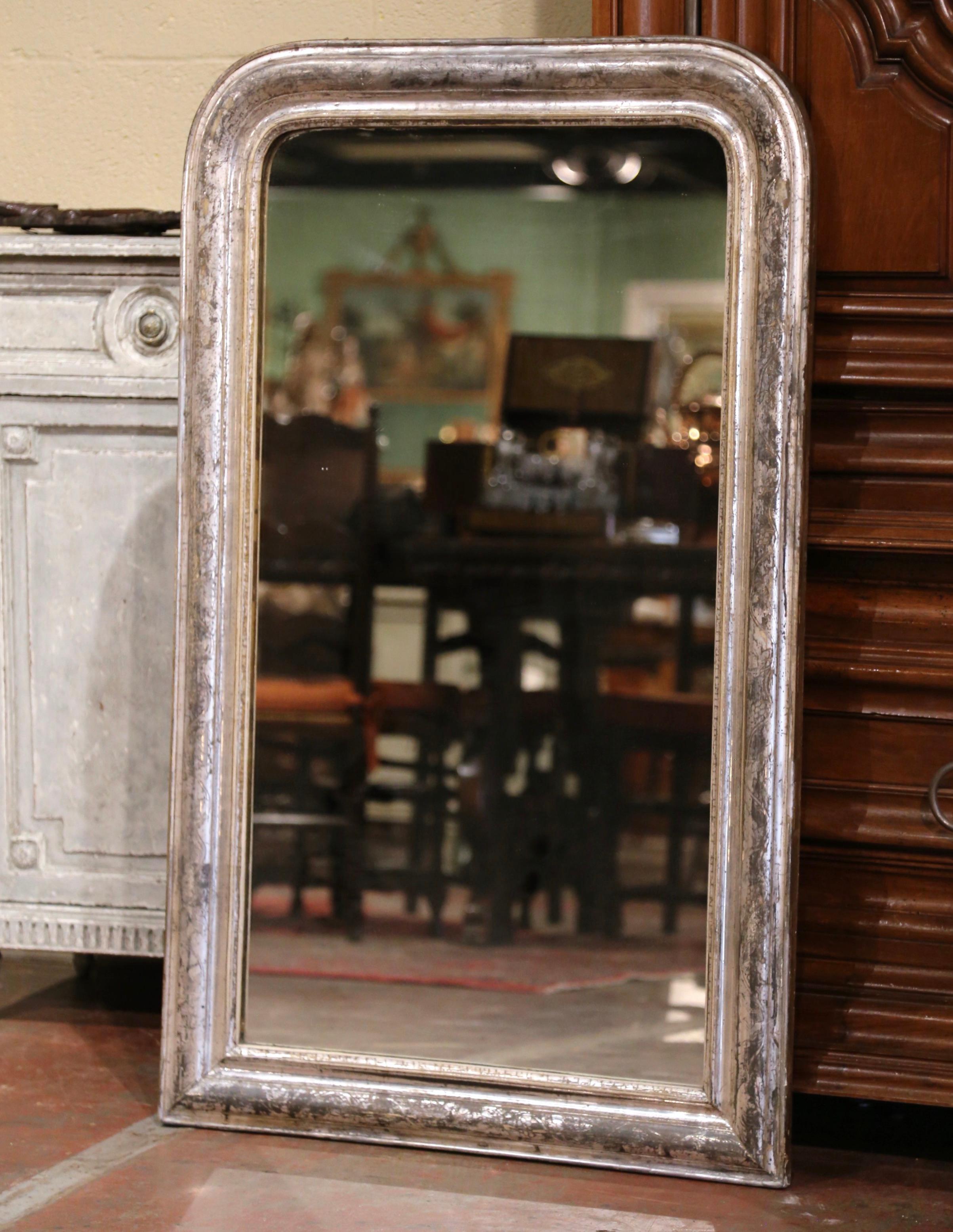 Crafted in the Burgundy region of France, circa 1860, the large antique mirror has traditional, timeless lines with rounded corners. The rectangular frame is decorated with a luxurious silver leaf finish over a discrete engraved two-tone foliage