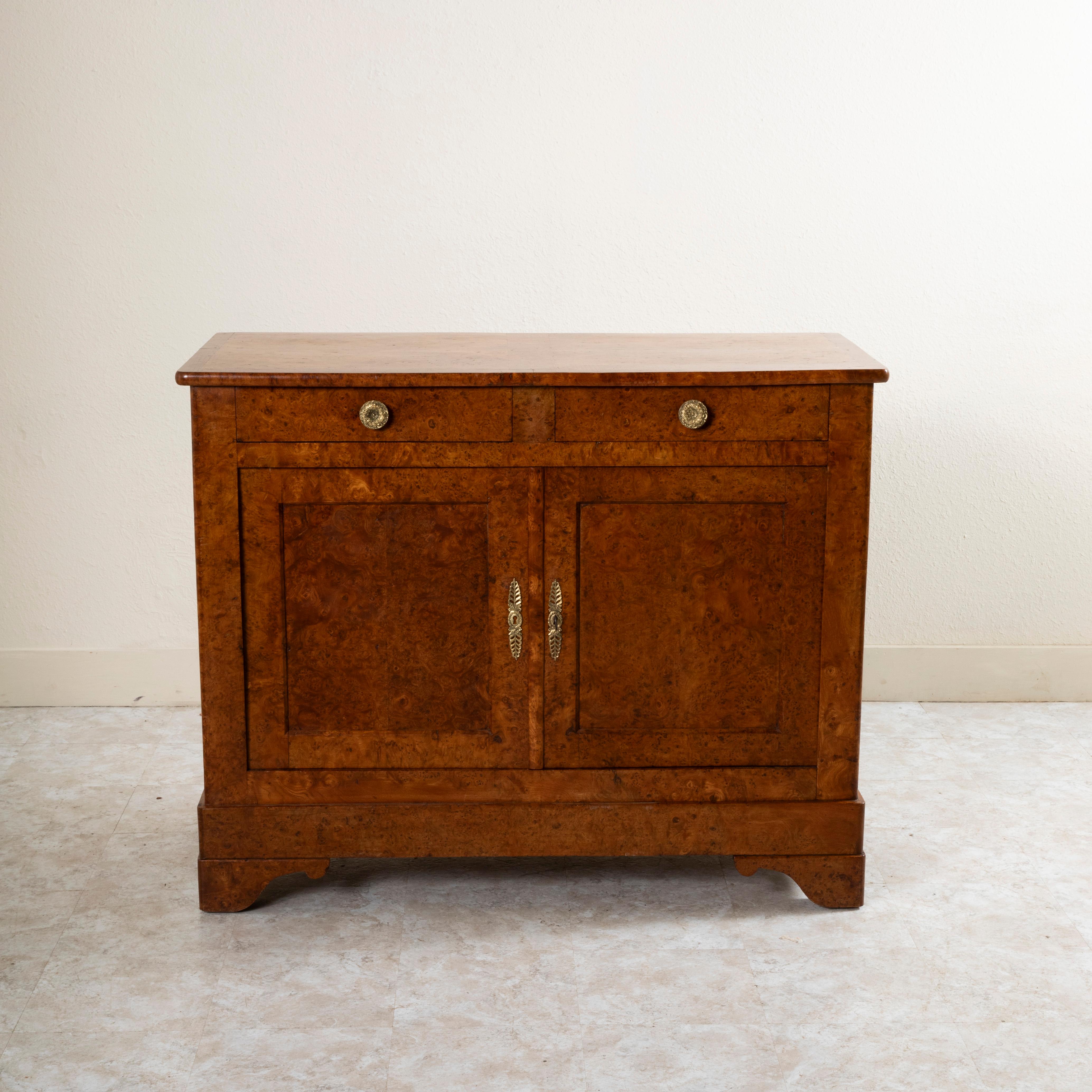 This Louis Philippe period buffet from the nineteenth century is constructed of solid burl elm. It features two upper drawers fitted with bronze drawer pulls detailed with a central rosette, shells, flowers and scrolling. Two lower doors open to
