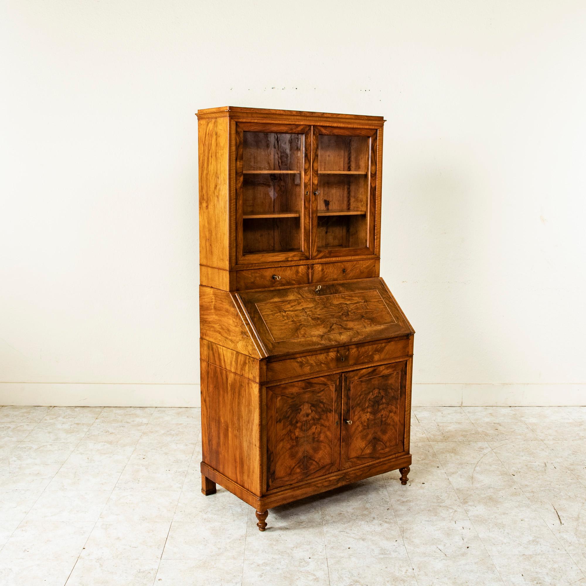 This nineteenth century French Louis Philippe period secretary is constructed of book matched burl walnut. The piece features a drop front gold tooled green leather writing surface with four interior drawers. The upper display cabinet has two doors