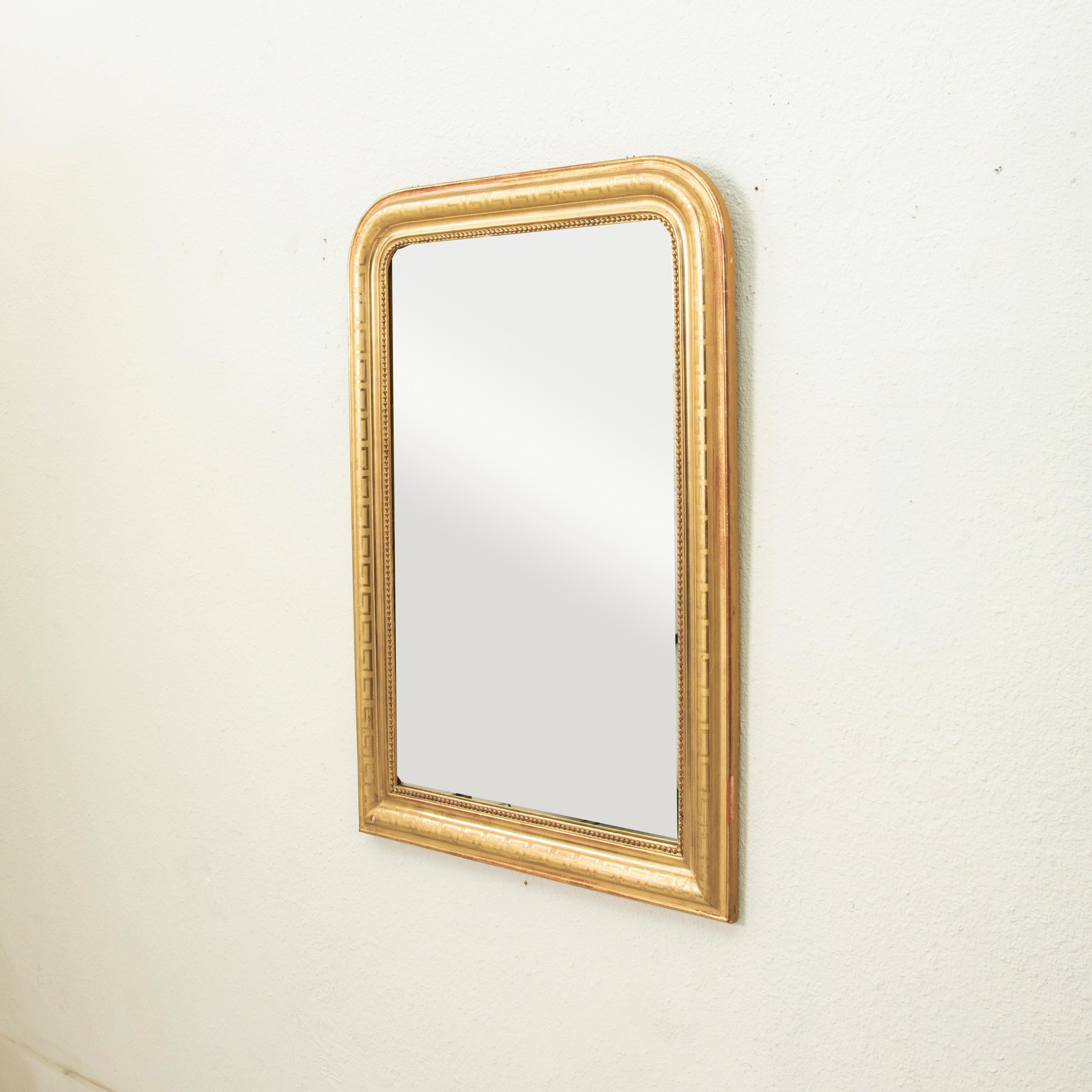 Questo specchio in legno dorato in scala ridotta del periodo Louis Philippe, risalente al XIX secolo, presenta una cornice a cuscino con un sottile motivo a chiave greca inciso e un bordo interno di perline sottili. L'ossido di ferro originale sotto