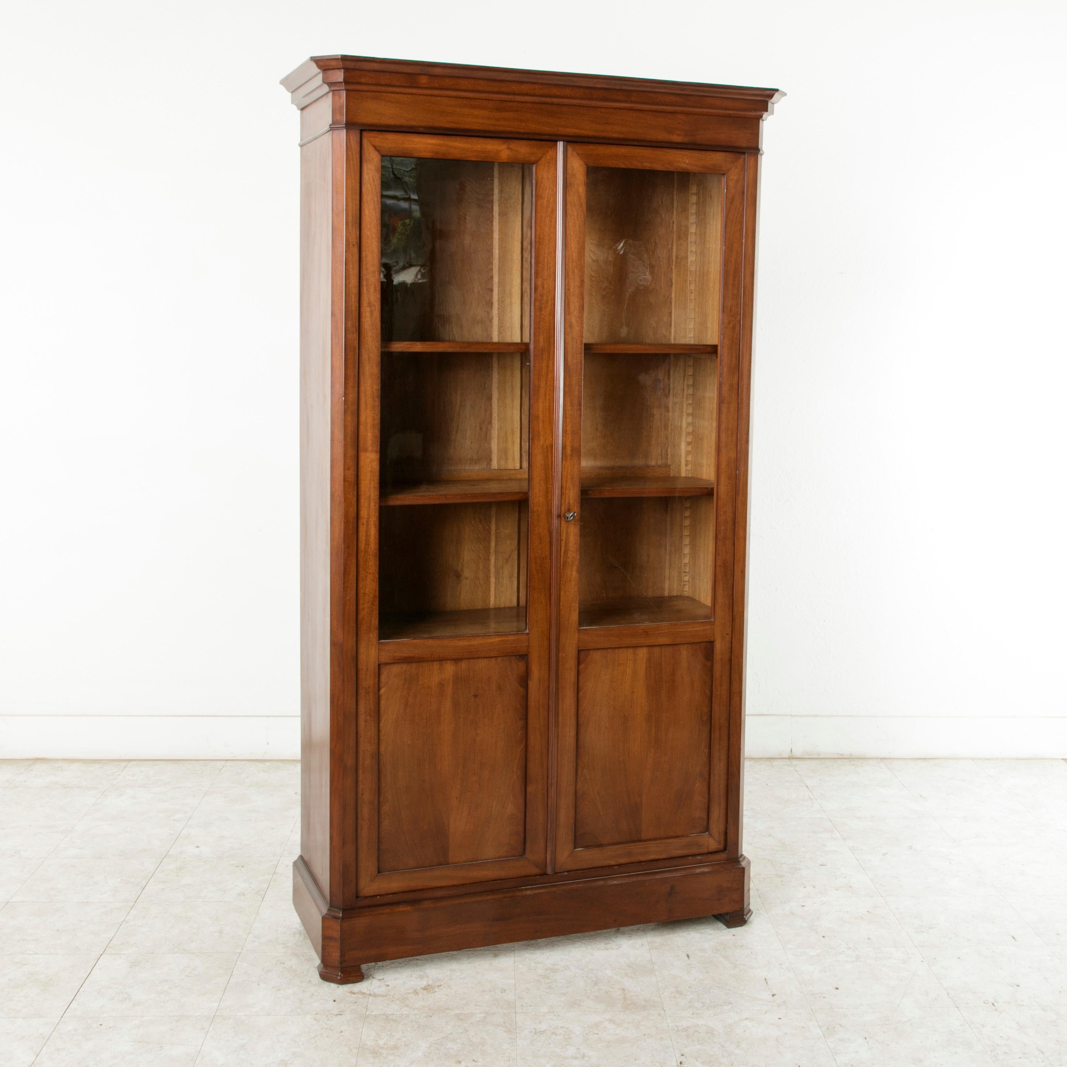 This 19th century Louis Philippe period mahogany bibliothèque, bookcase, or vitrine features simple, handsome lines and two doors inset with their original glass. It has four adjustable interior shelves for ample storage and display space. The warm