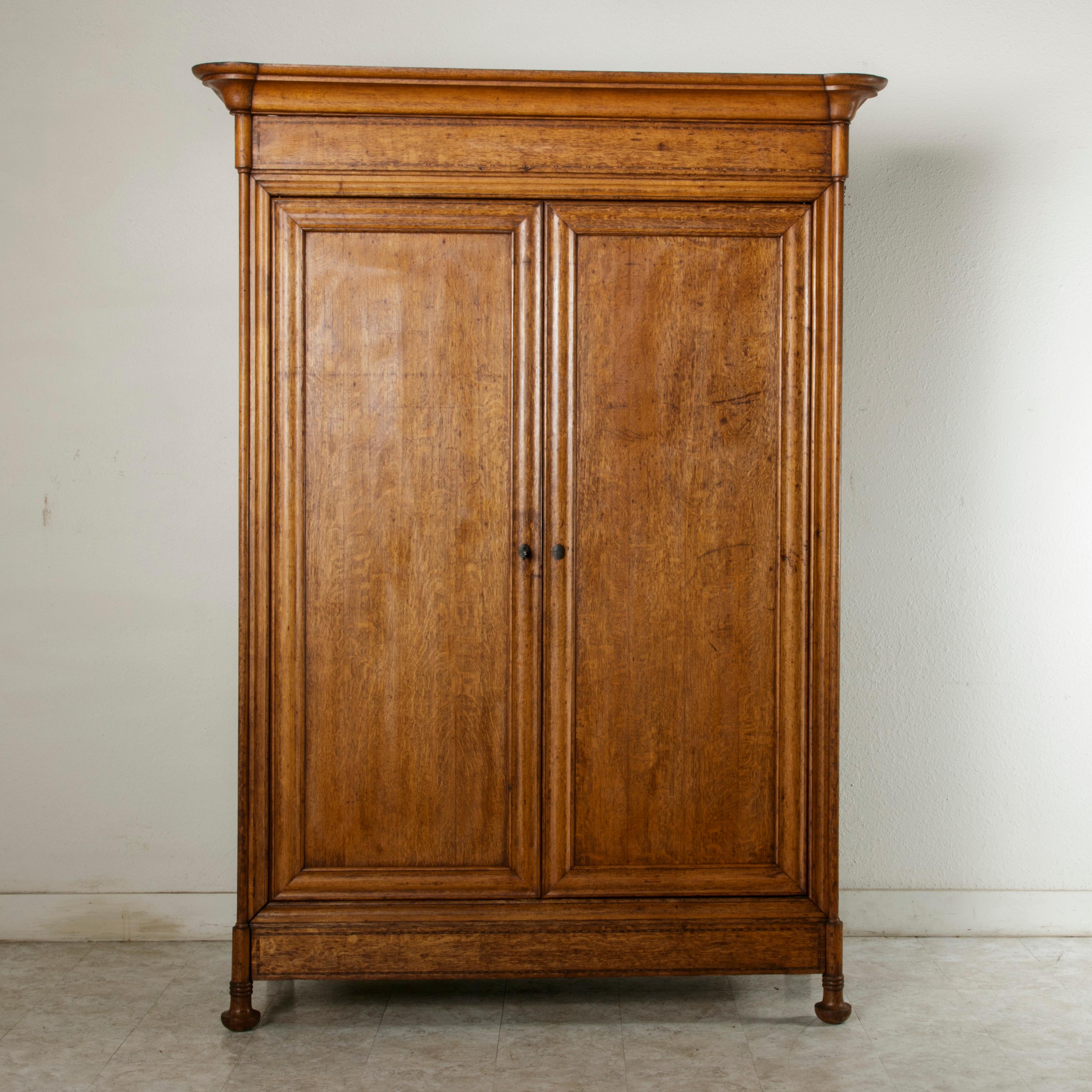 Found in Paris, this large scale Louis Philippe period armoire from the mid-19th century is constructed of solid oak and features rounded front corners and a subtle geometric border of inlaid ebonized pear wood on the facade. The armoire stands
