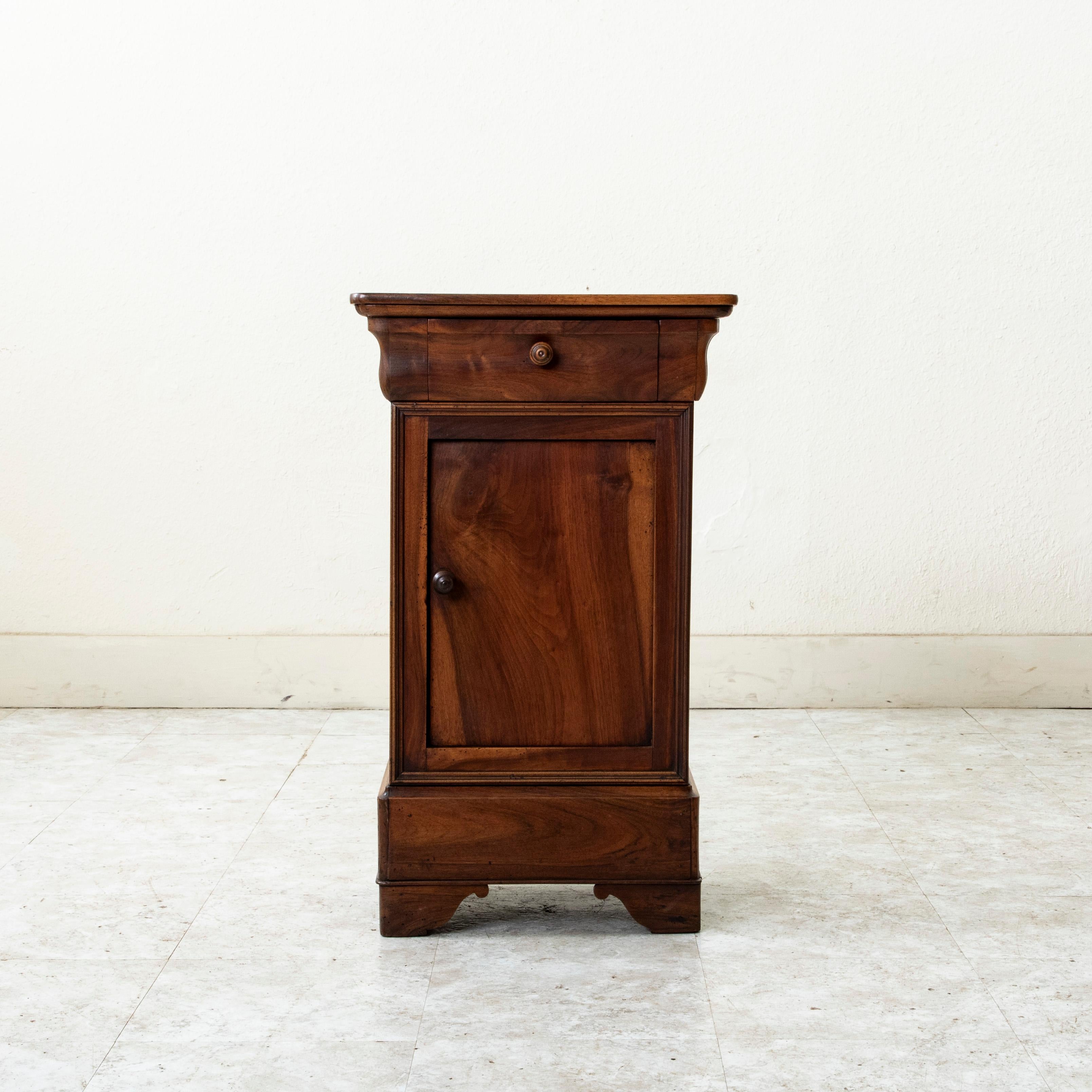 Cette table de nuit ou table d'appoint d'époque Louis Philippe, datant du XIXe siècle, est construite en noyer massif et comporte une seule porte et un tiroir supérieur à queue d'aronde. Le tiroir s'intègre parfaitement dans le tablier et est doté