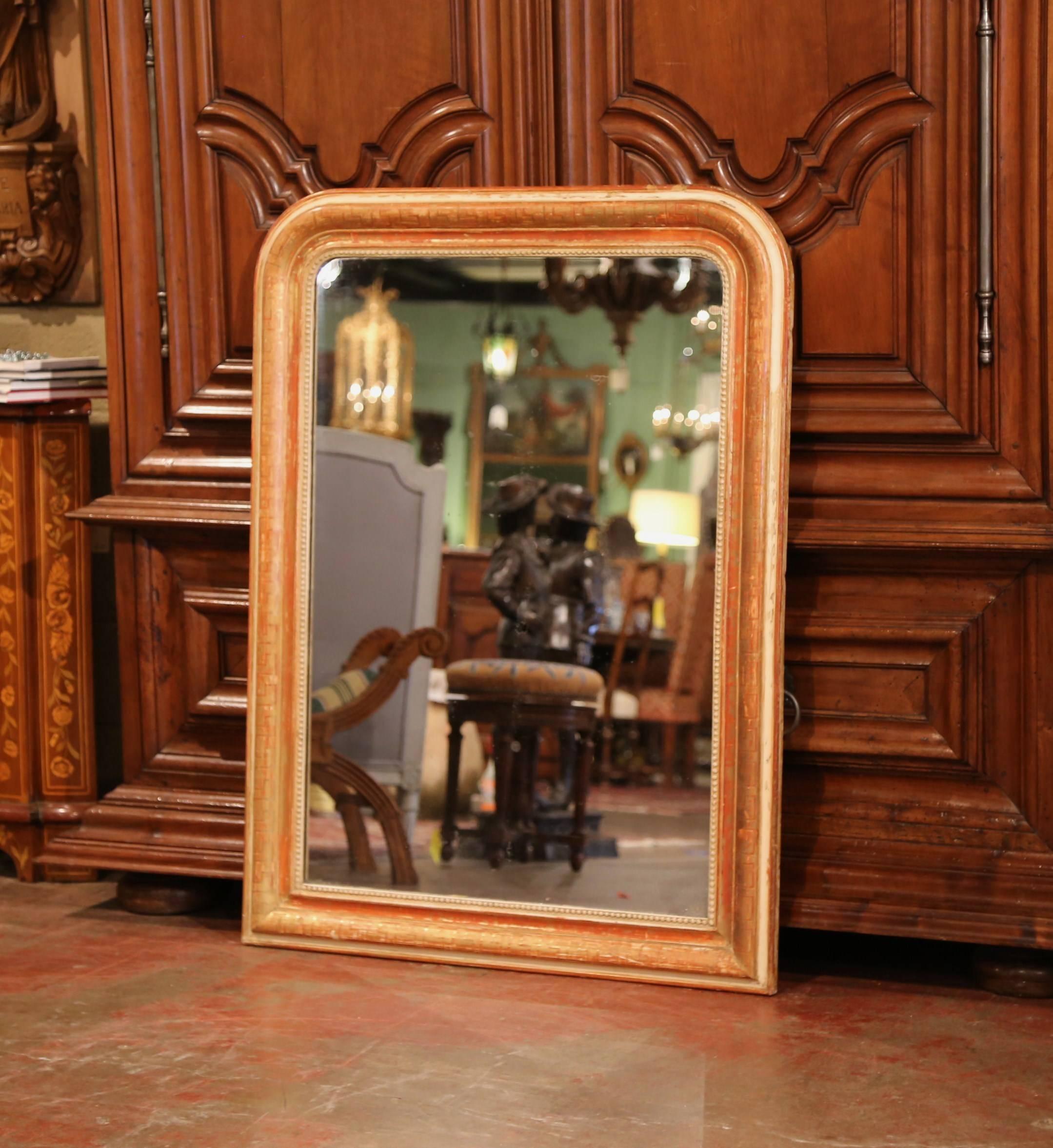 This elegant antique wall hanging mirror was crafted in France, circa 1860. The traditional Louis Philippe mirror features a two-tone red and gold leaf finish with white gesso, further embellished by engraved Greek key motif around the frame. The