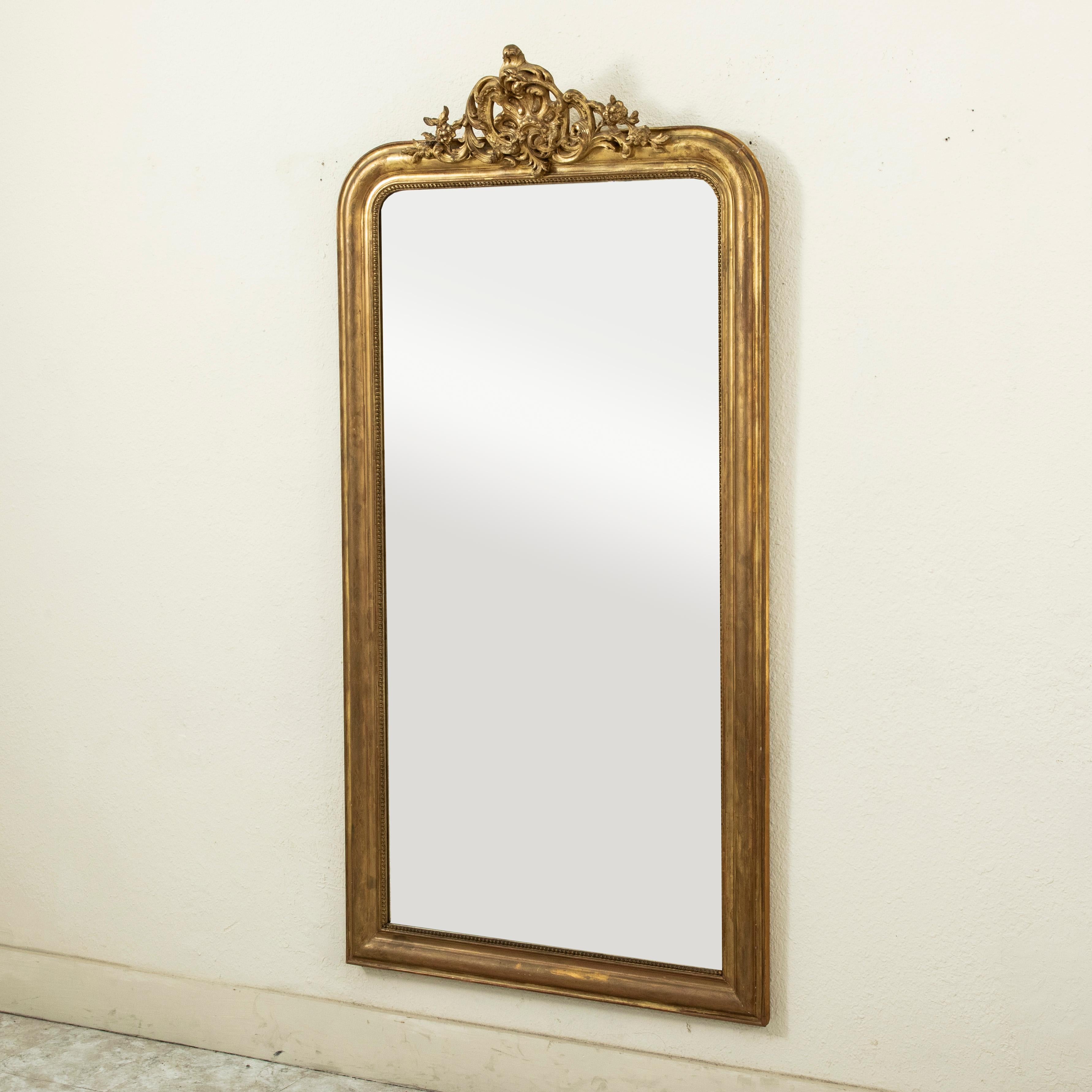 Este espejo de madera dorada de mediados del siglo XIX, de estilo Louis Philippe, presenta su cristal de mercurio biselado original rodeado por un marco almohadillado detallado con sutiles incisiones de motivos florales y un borde interior de fina