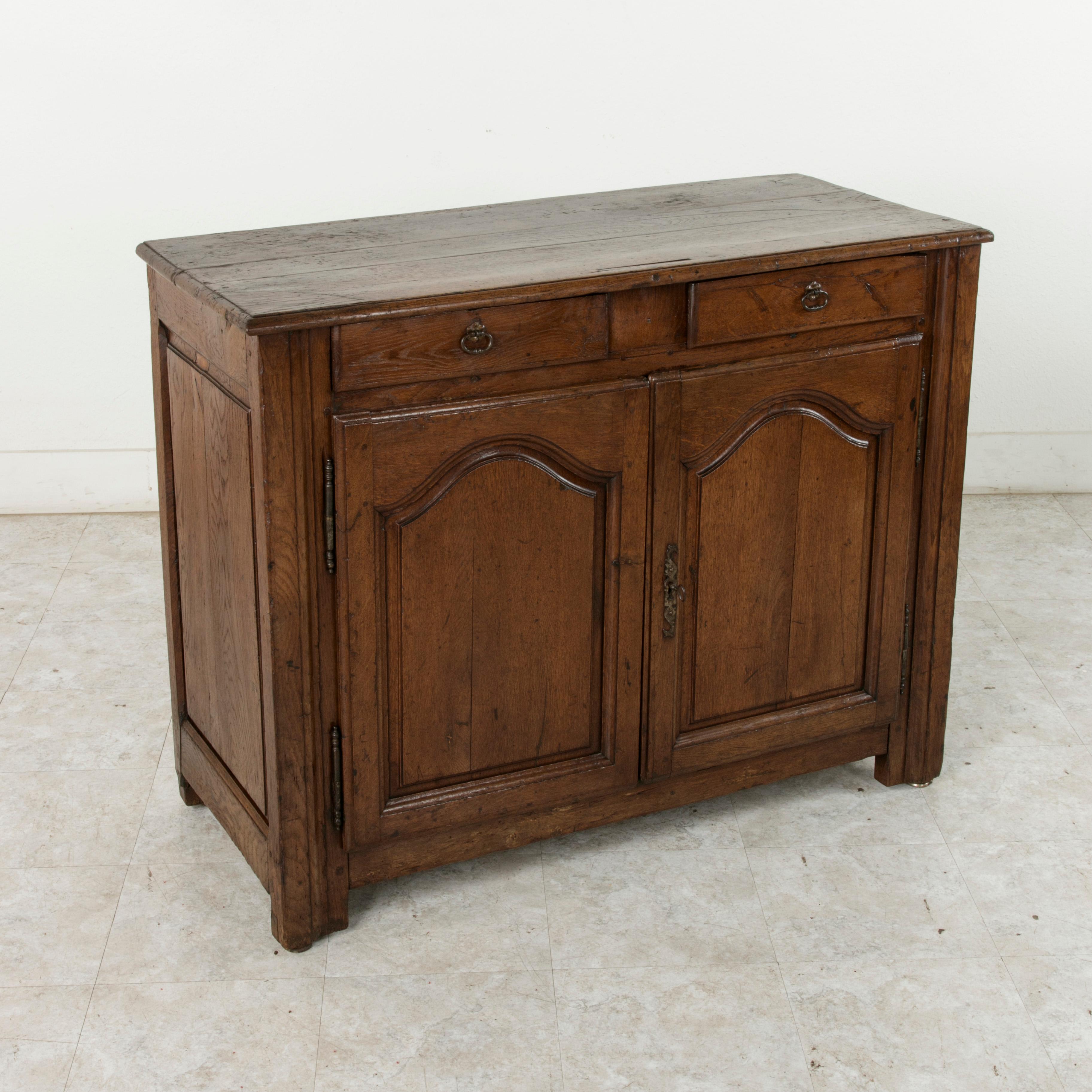 This mid-19th century French Louis XIV style artisan-made oak buffet or sideboard from the region of Normandy, France, features paneled sides of hand pegged mortise and tenon construction. The beveled top rests above two drawers fitted with iron