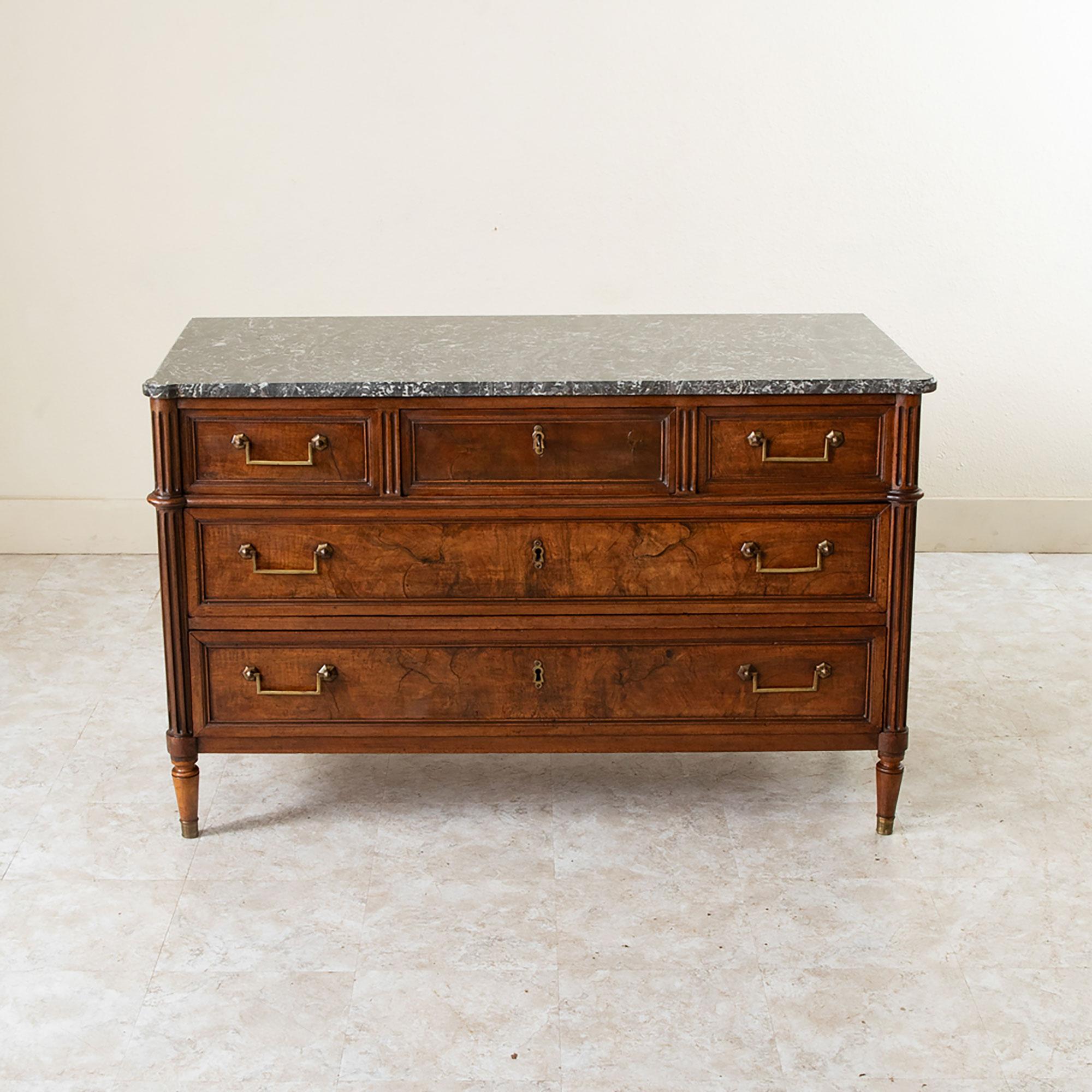 This mid nineteenth century French Louis XVI style walnut commode or chest of drawers features a beveled Saint Anne marble top and fluted rounded corners. Its five drawers of dovetail construction are fitted with classic bronze squared drop handle