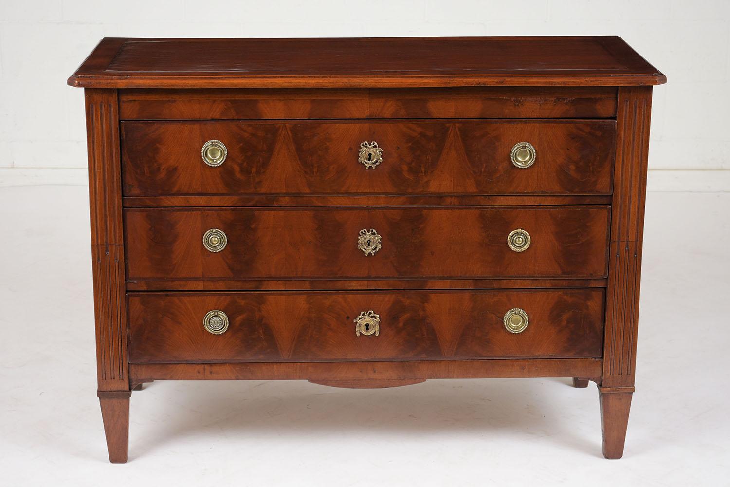 This 1850s French Louis XVI Style Commode is made of mahogany wood finished in a rich color stain with a polished finish and is in good condition. The dresser features a wooden top with a beveled edge, three drawers covered in veneers with inlaid