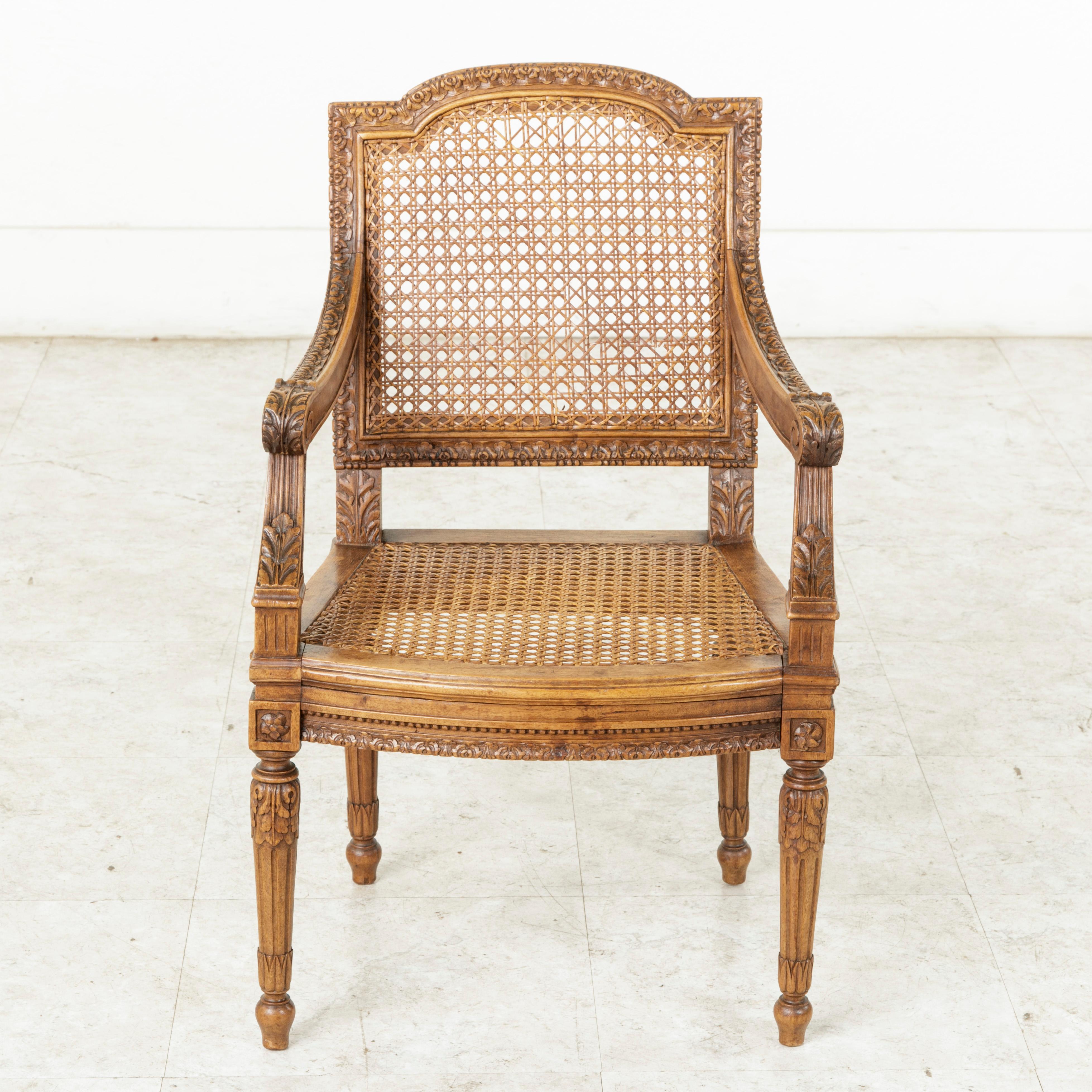 This mid-19th century French walnut child's chair features Classic Louis XVI style hand carvings and a caned seat and seat back in excellent condition. Carvings of stylized acanthus leaves detail the seat back and scrolled arm rests. Rosettes adorn