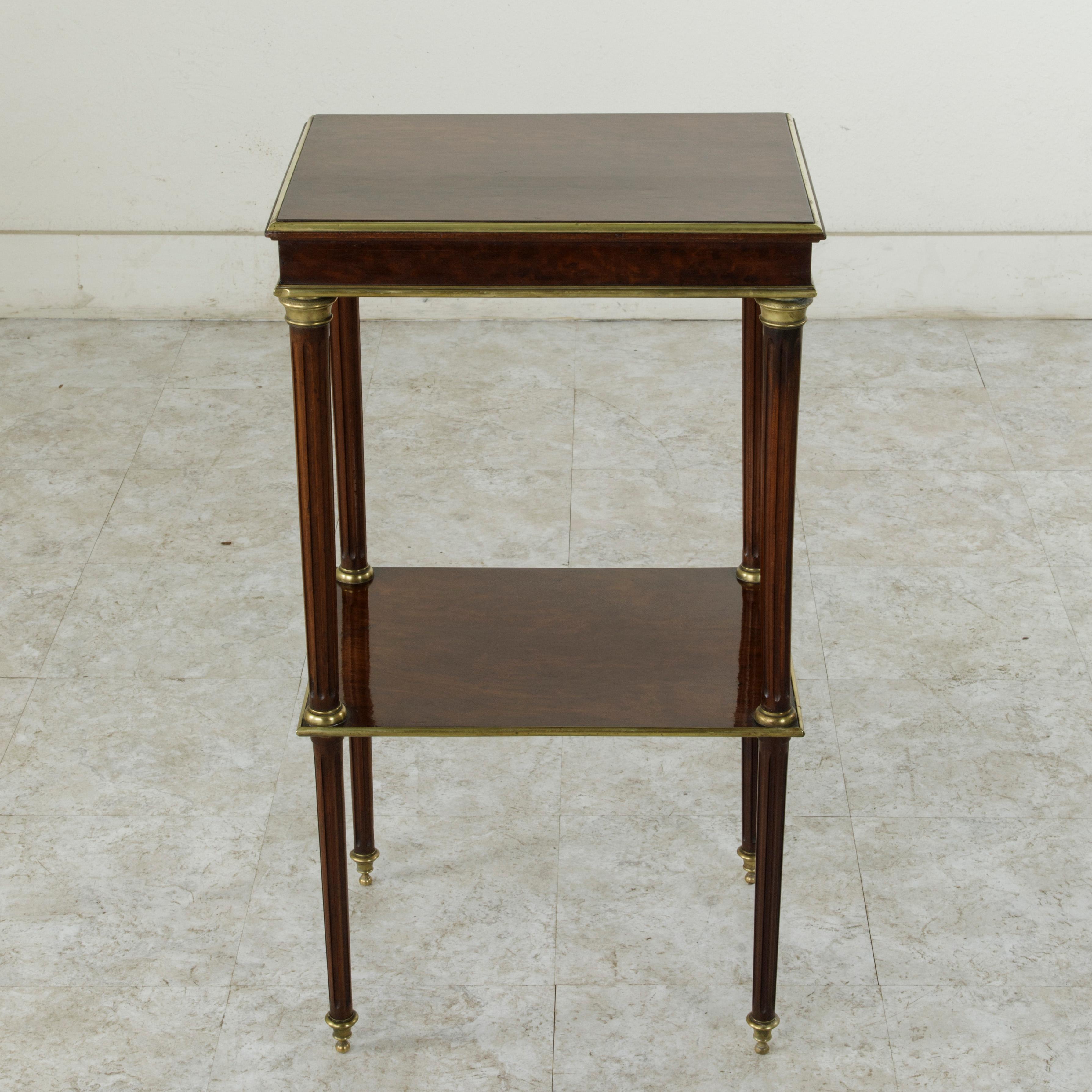 This mid-19th century French Louis XVI style side table constructed of rich plum pudding mahogany features bronze trim that surrounds the piece on all sides. The top rests on tapered fluted legs finished with bronze sabots. A lower shelf also