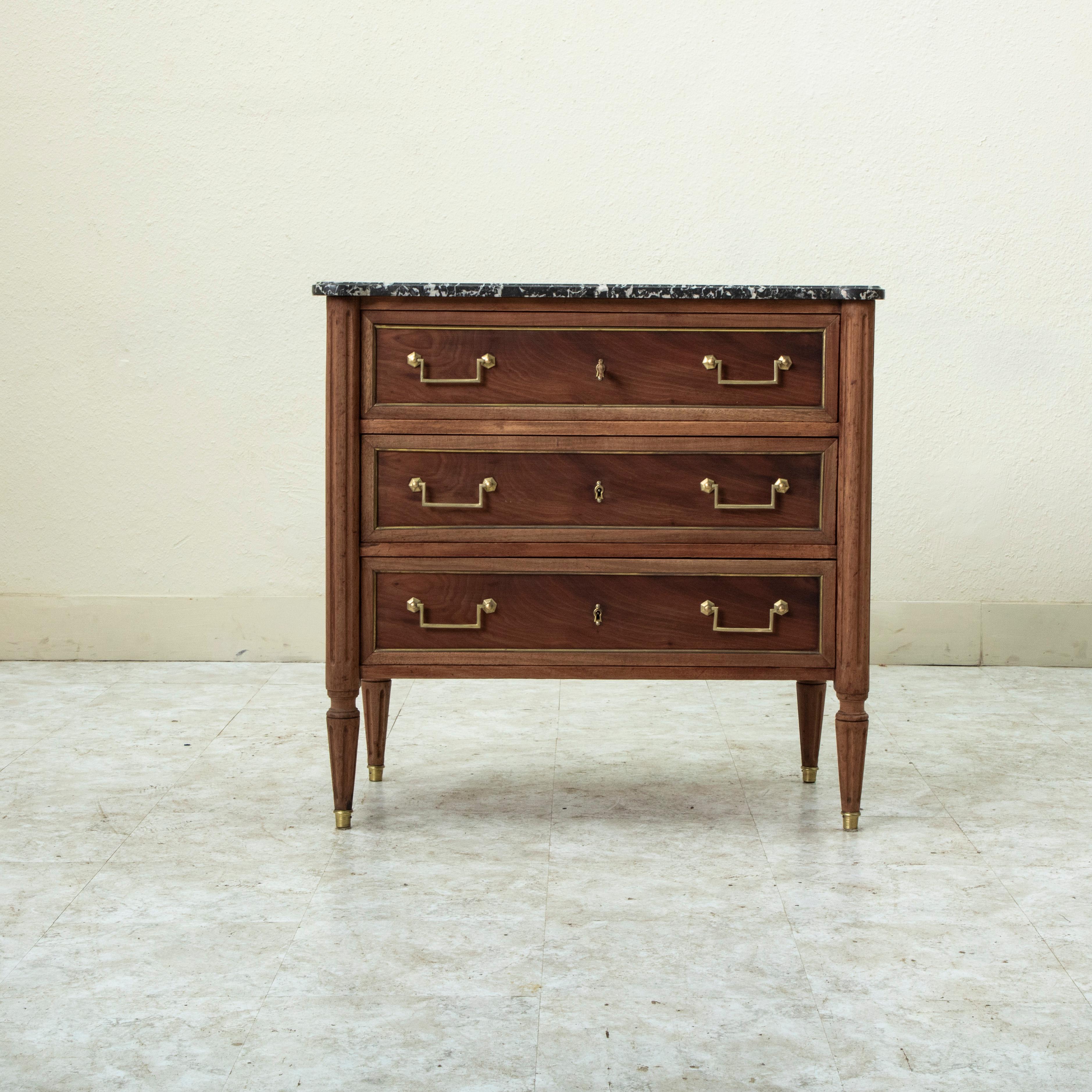 Measuring only 33 inches wide, this small scale nineteenth century French Louis XVI style walnut commode or chest of drawers features a Saint Anne marble top and fluted rounded corners. Its three drawers of dovetail construction are detailed with