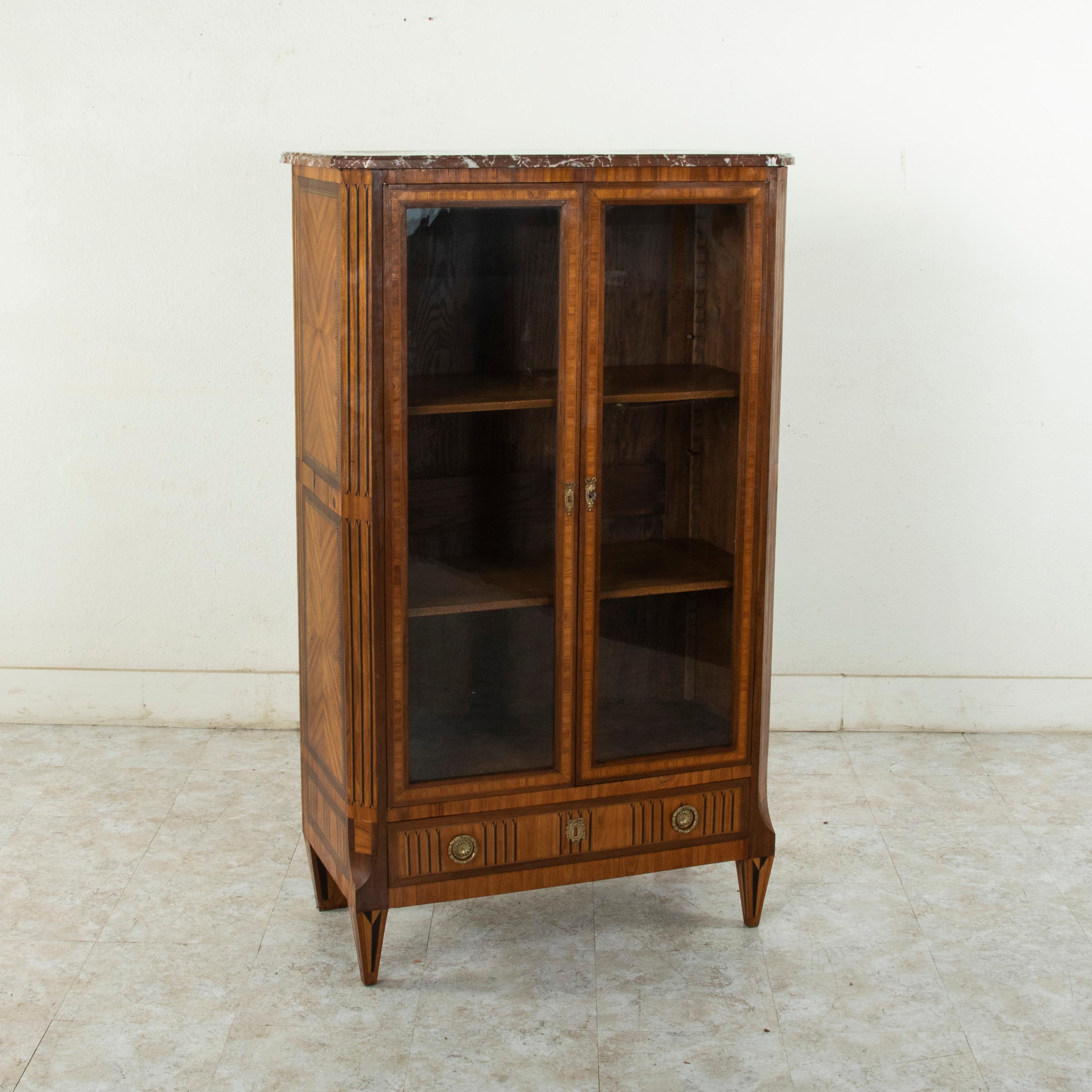 This mid-19th century Louis XVI style walnut marquetry vitrine features a beveled rose colored marble top. Trompe l'oeil fluting at the corners of the cabinet is created by inlaid bands of pear wood and ebonized pear wood. This motif is repeated on