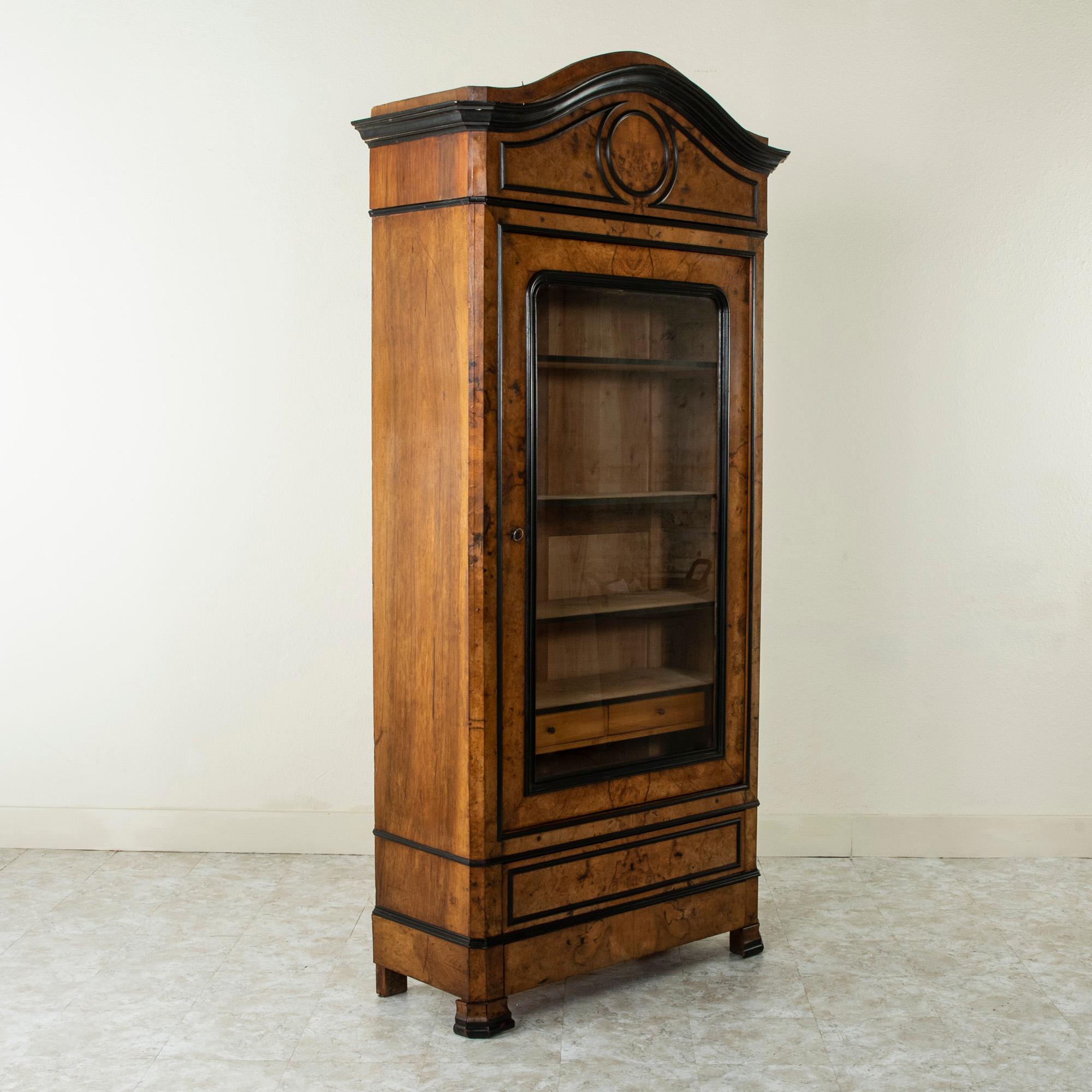 This mid-19th century French Napoleon III period vitrine or bookcase is constructed of burl walnut and features clean simple lines. Providing an elegant contrast, the piece is trimmed in ebonized pearwood. Of an unusual size with its narrow width of
