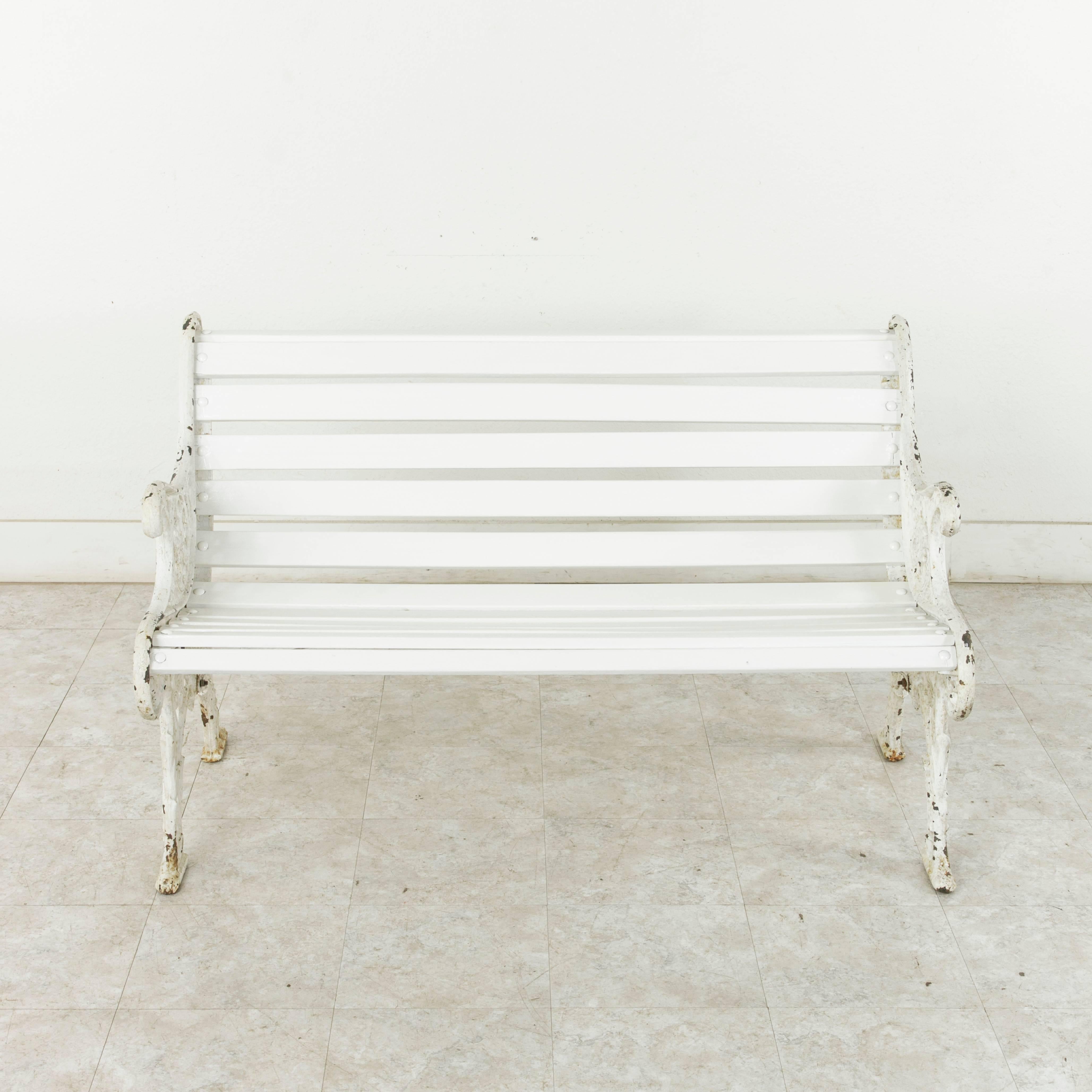 This mid-19th century Napoleon III period park bench from Normandy, France, features a curved seat and back formed by wooden slats that are bolted to the two cast iron ends. The quintessential French park bench, the intricate ironwork includes a